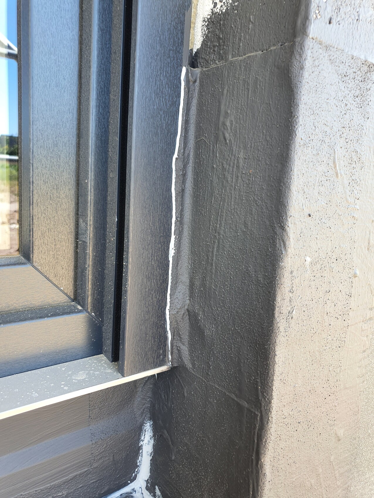 Fensterrahmen an grauer Wand; weiße Dichtstoff-Fuge mit sichtbarem Riss.