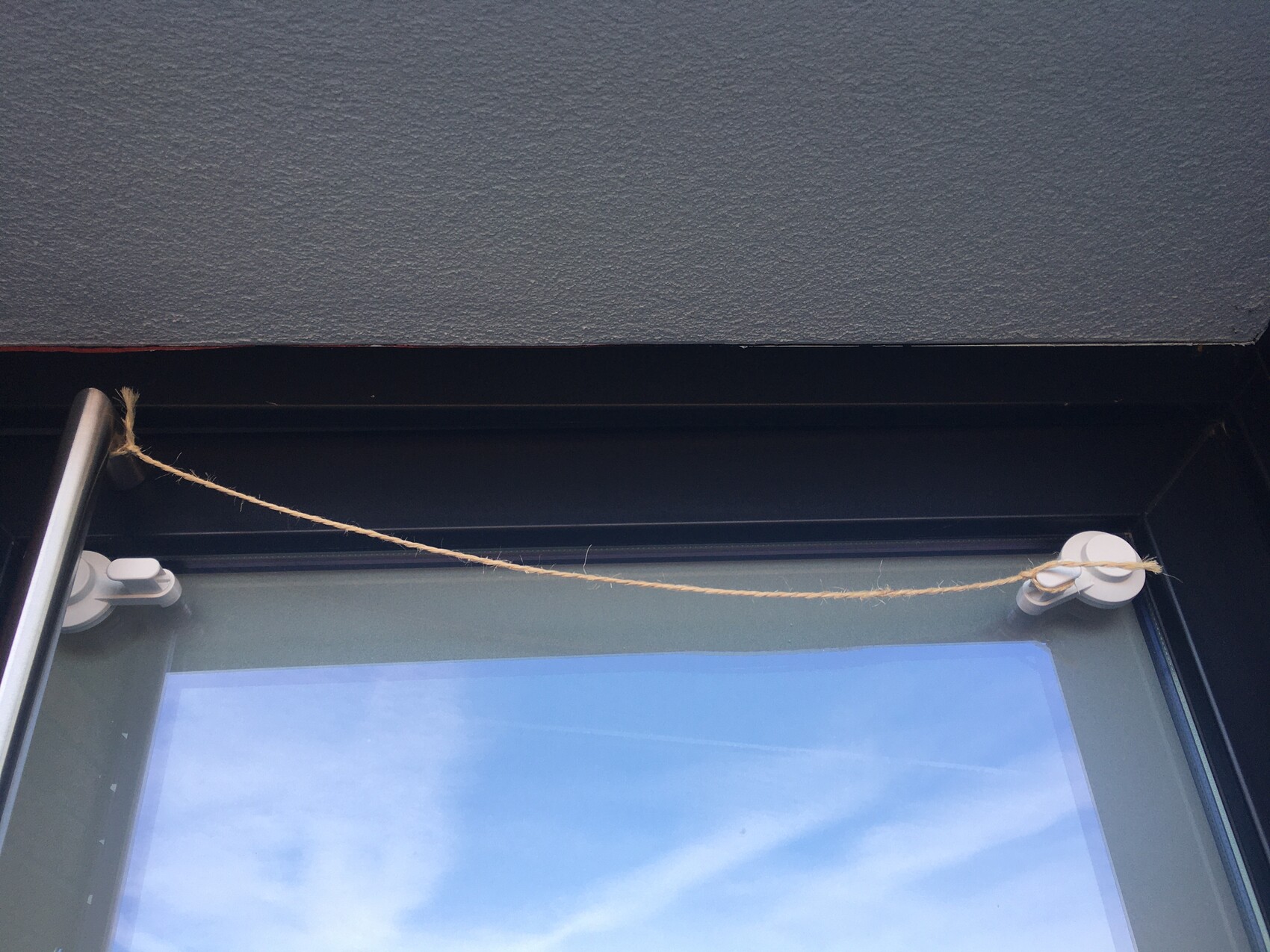Juteschnur spannt sich von links nach rechts über das Fenster, befestigt an zwei weißen Halterungen.