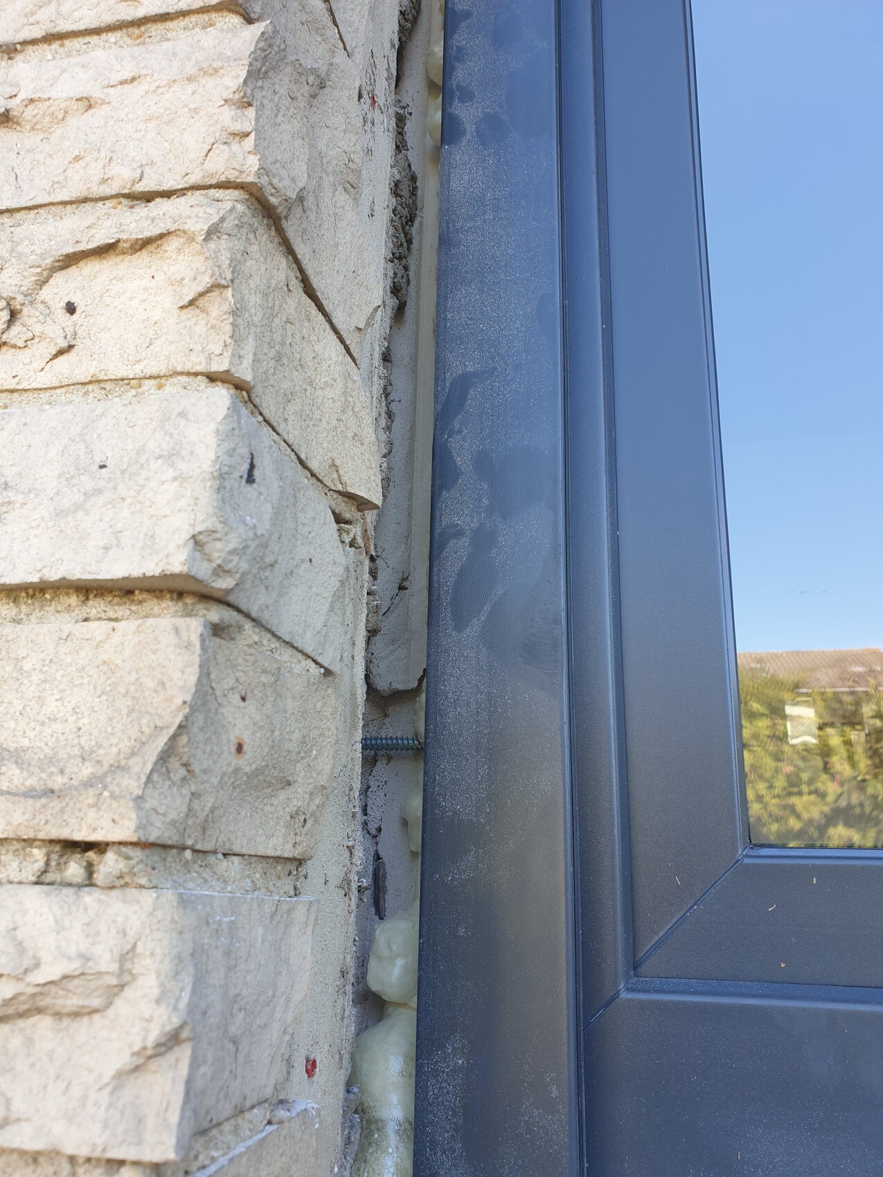 Außenansicht: Steinwand neben dunkelblauem Fensterrahmen mit sichtbarem Dämm-Schaum.