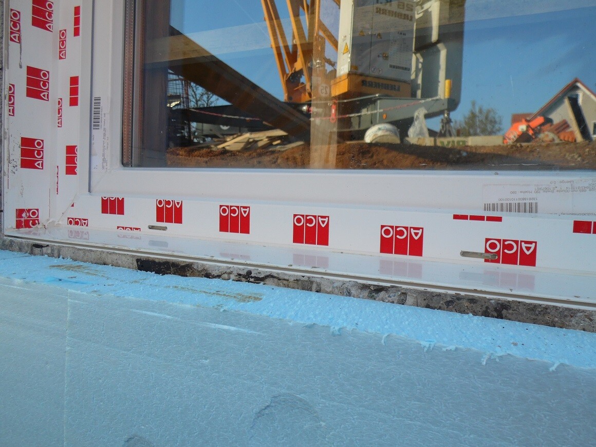 Fensterrahmen auf Baustelle mit blauer Dämmung darunter und Baugeräten im Hintergrund