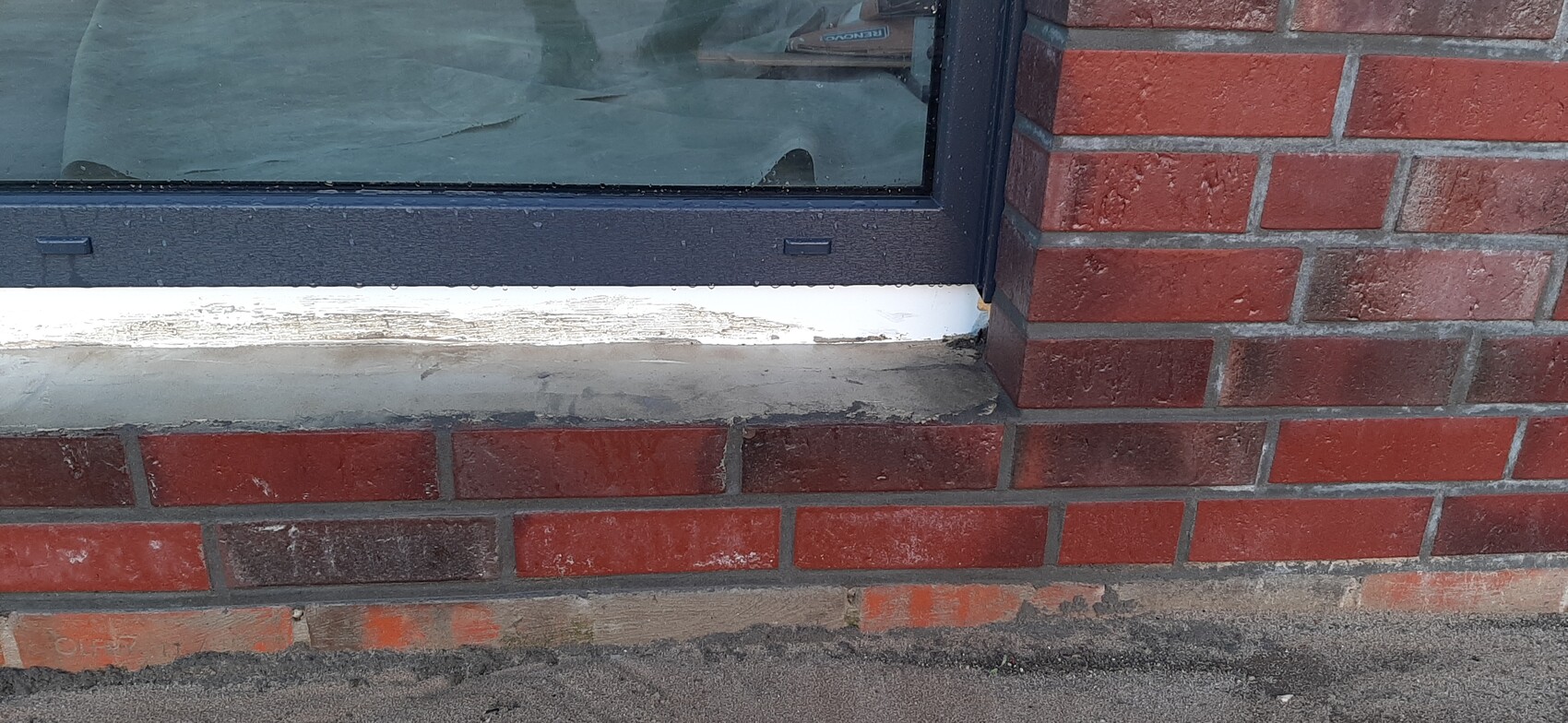 Außenansicht eines Fensters in rotem Backstein, dunkelblauer Rahmen und weißer Fensterbank.