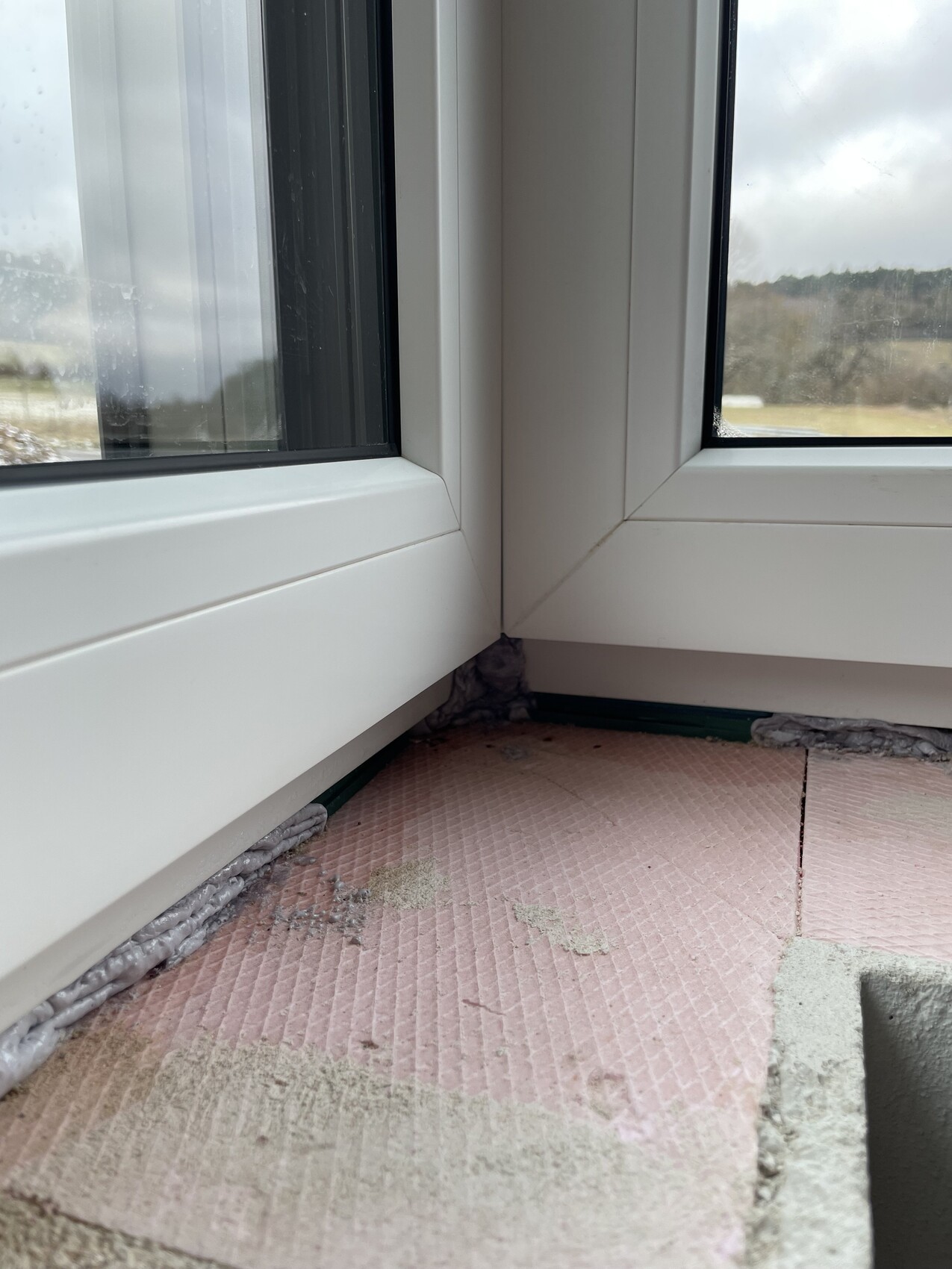 Weisser Kunststofffensterrahmen mit sichtbarer Daemmung und Dichtmaterial am Bodenbereich