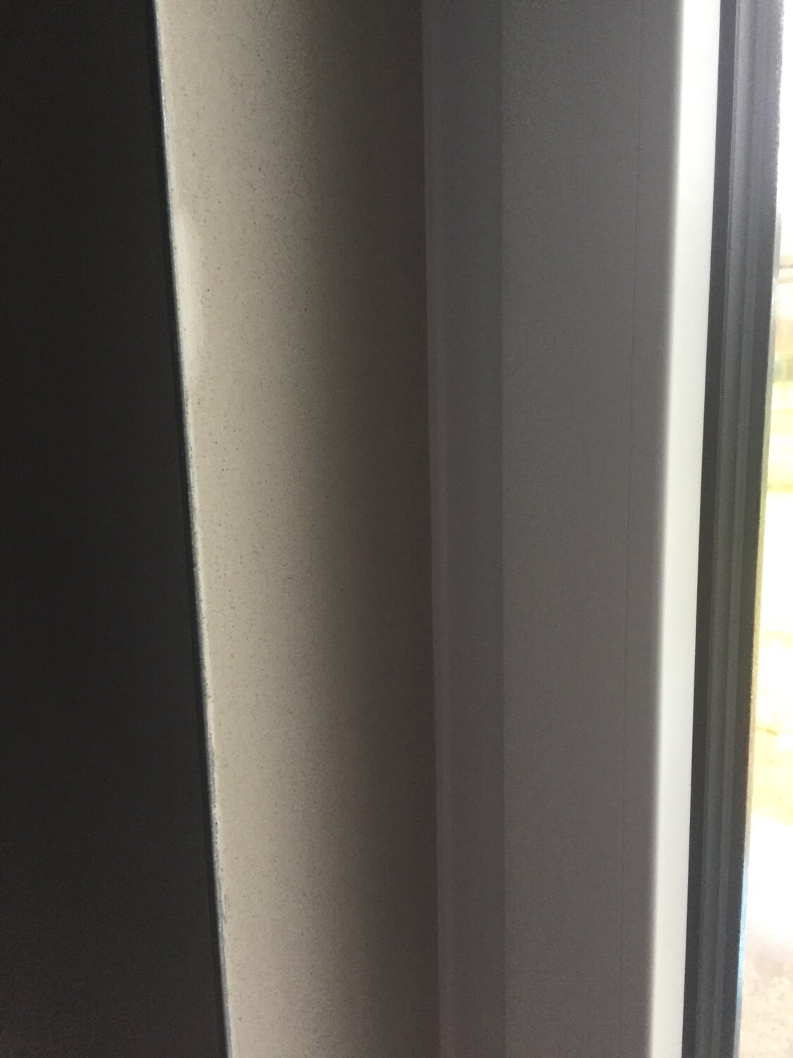 Nahaufnahme eines Fensterrahmens mit dunkler Wand links und heller Leiste; Außenbereich sichtbar