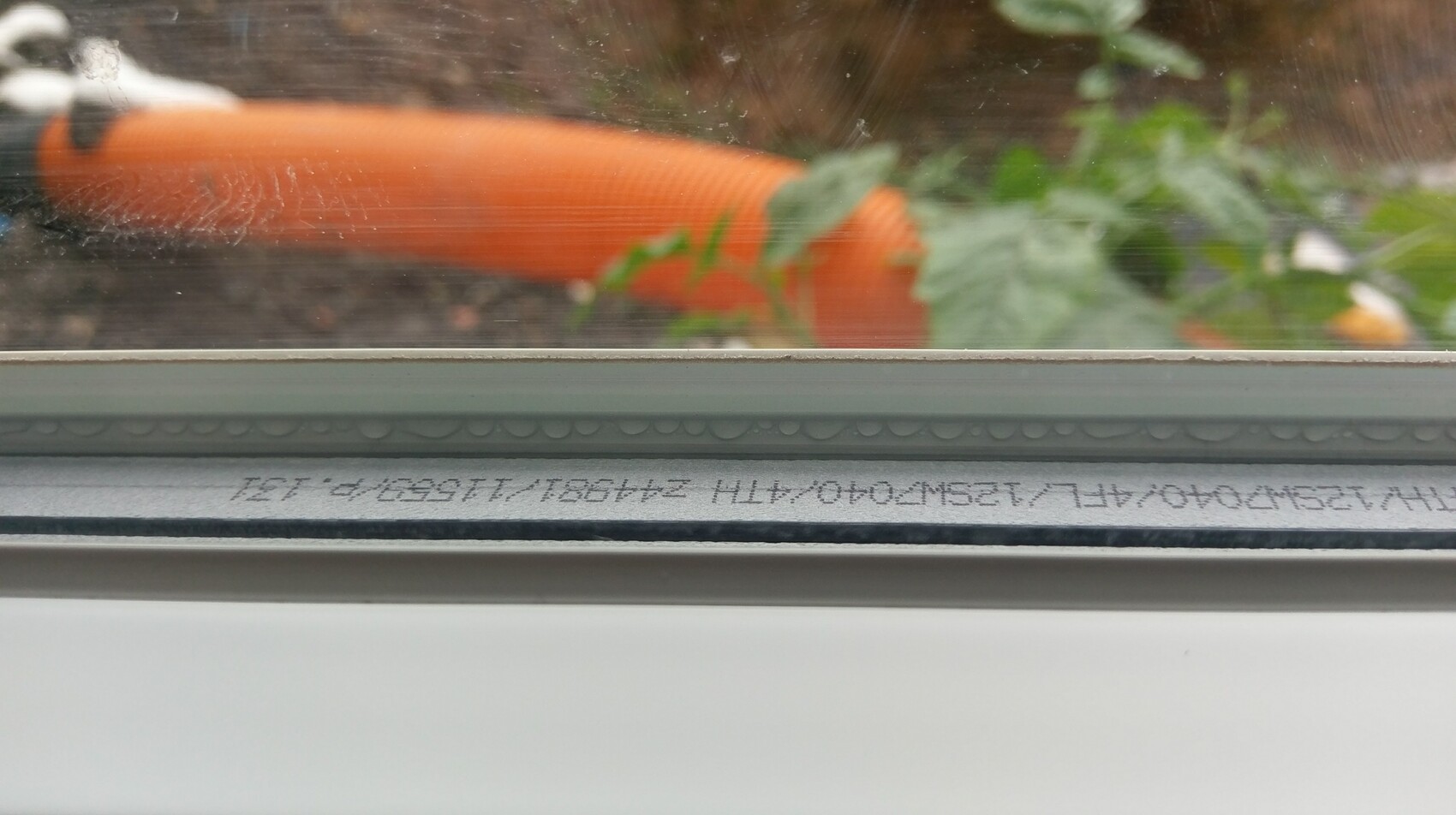 Nahaufnahme eines Fensterrahmens mit Glas, Außenansicht Rohr und grünen Pflanzen sichtbar