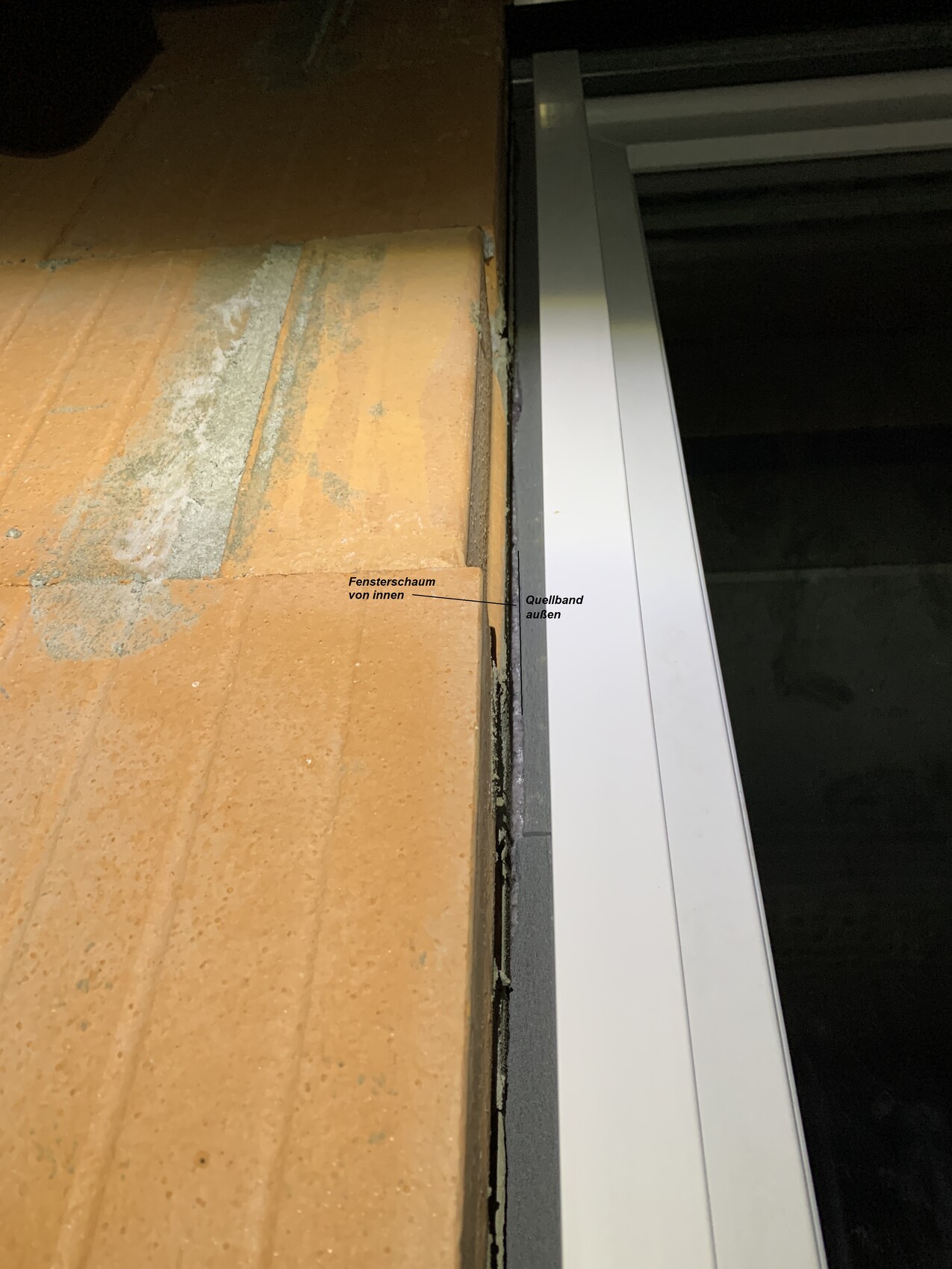 Fensterrahmen an Ziegelwand; Fensterschaum innen und Quellband außen sichtbar.