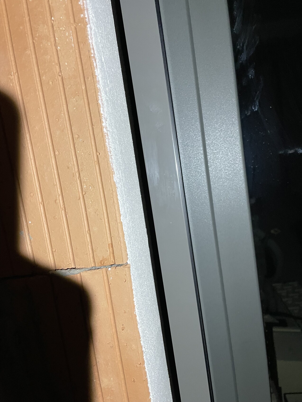 Nahaufnahme eines hellgrauen Fensterrahmens neben orange Backsteinwand