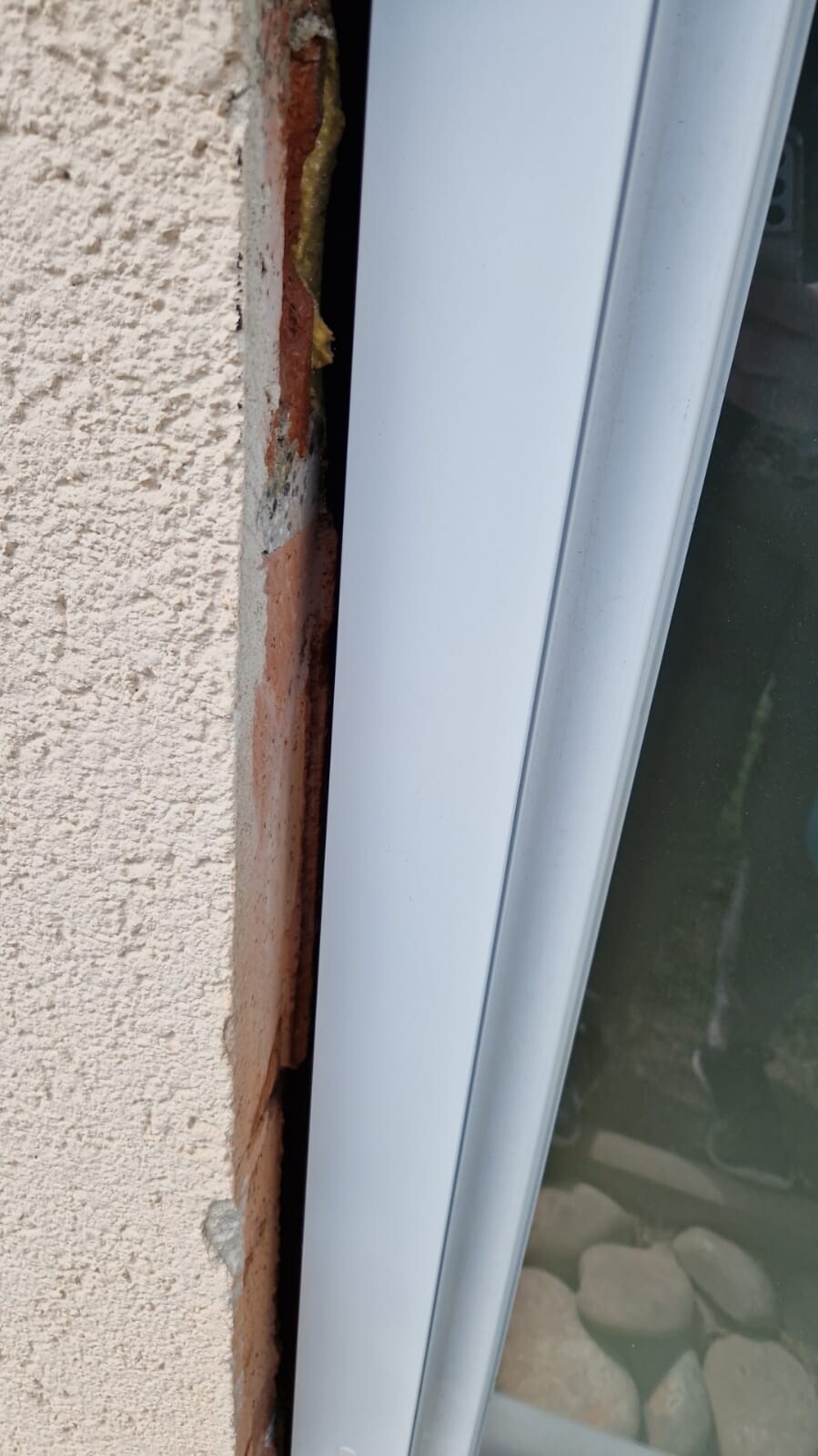 Fensterrahmen vor verputzter Außenwand; Spalt mit gelbem Dichtungs-Schaum und Putzbruch.