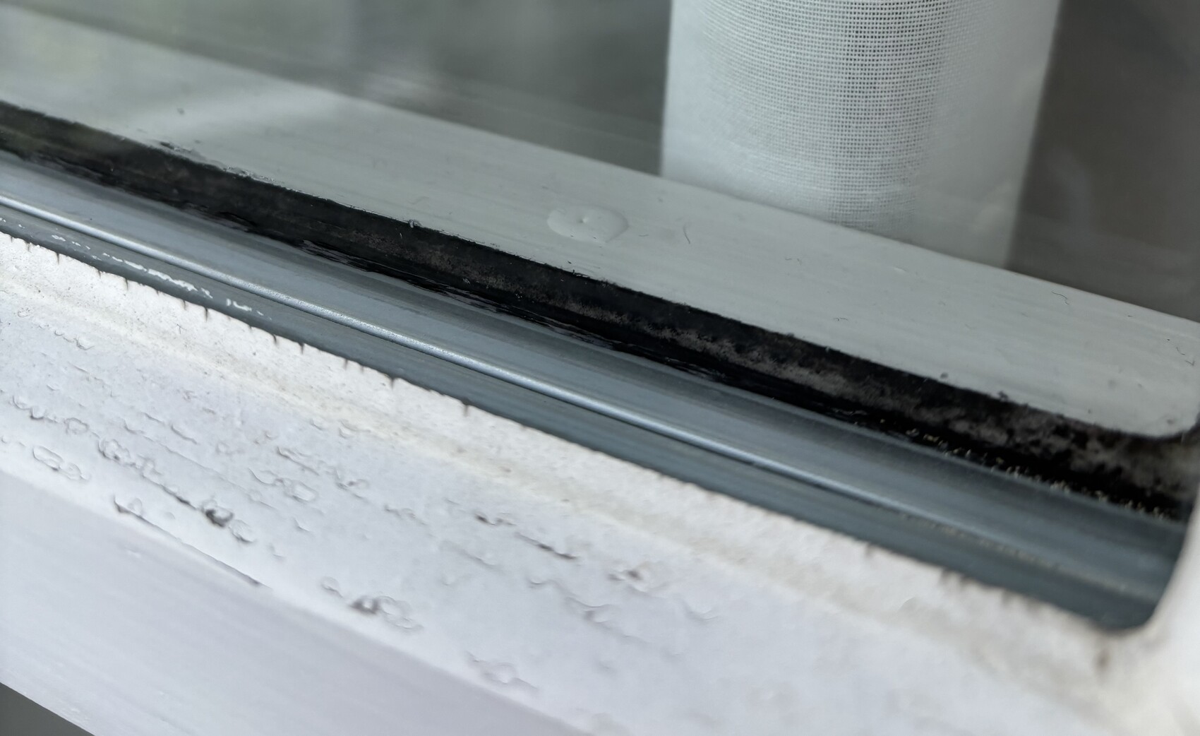 Nahaufnahme eines Fensterrahmens mit Dichtungsstreifen und Staub am unteren Rand.