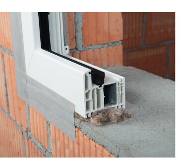 Nahaufnahme eines weißen Fensterrahmenprofils in einer Backsteinwand im Rohbau