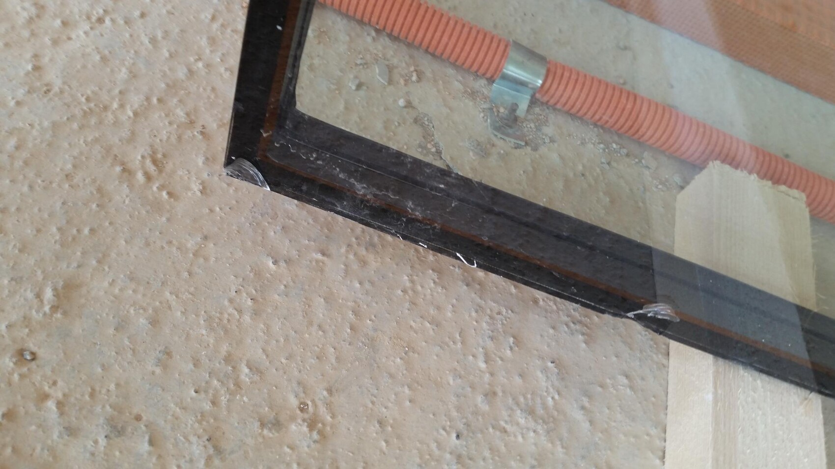 Fensterrahmen mit Glas auf Baustelle, daneben orange Kabelkanal.