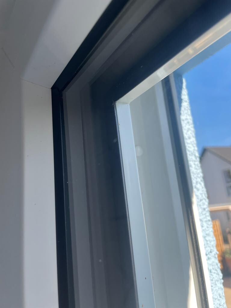 Innenansicht eines Fensterrahmens, Blick auf blauen Himmel und Nachbarhaus.