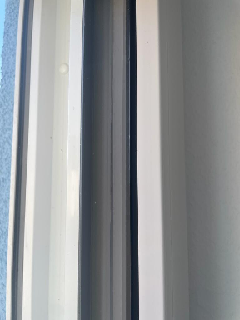 Nahaufnahme eines weißen Fensterrahmens mit dunklem Spalt; außen blaue Wand.
