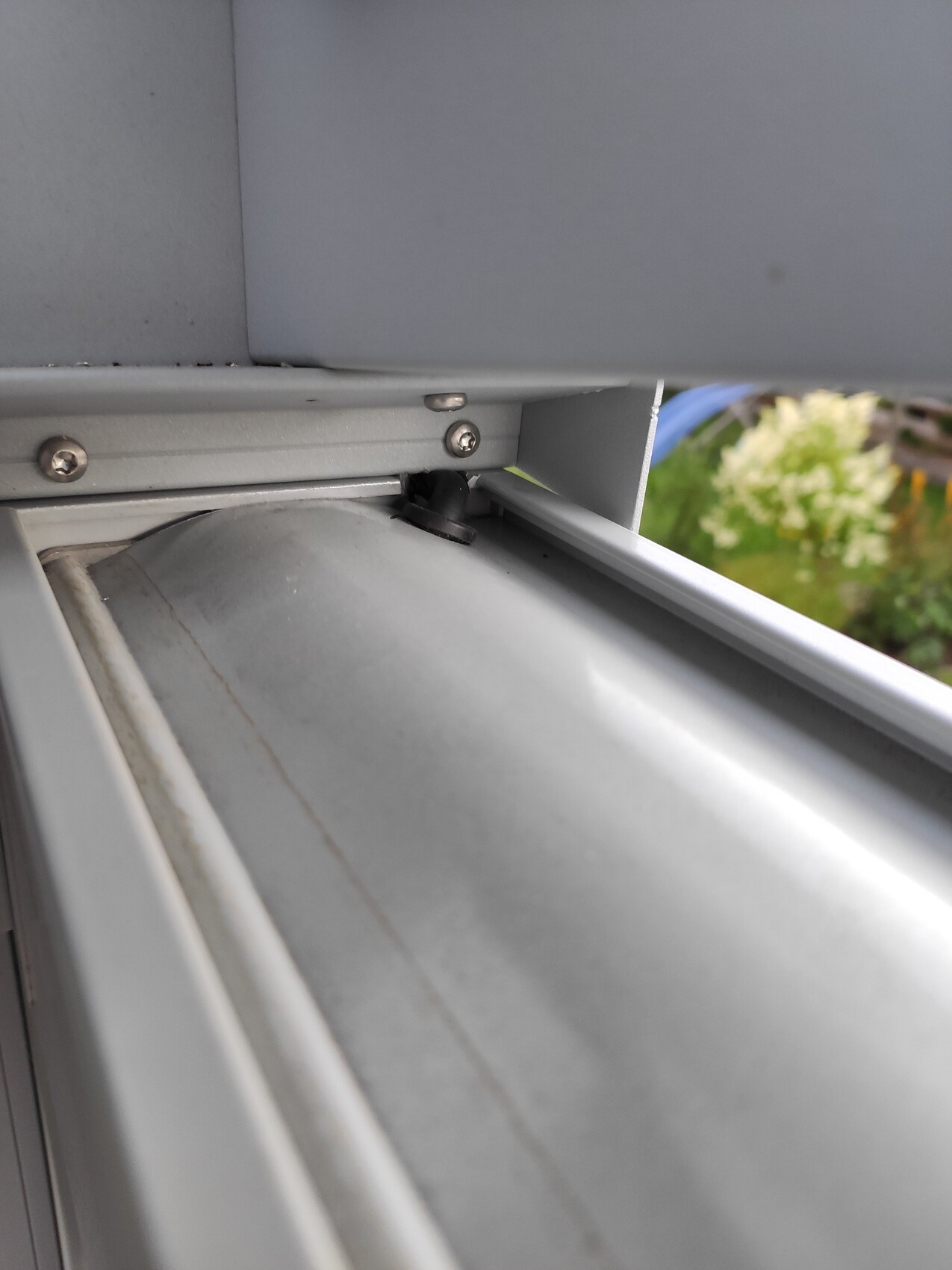 Nahaufnahme eines metallischen Fensterrahmens mit Schrauben und kleinem schwarzen Knopf.