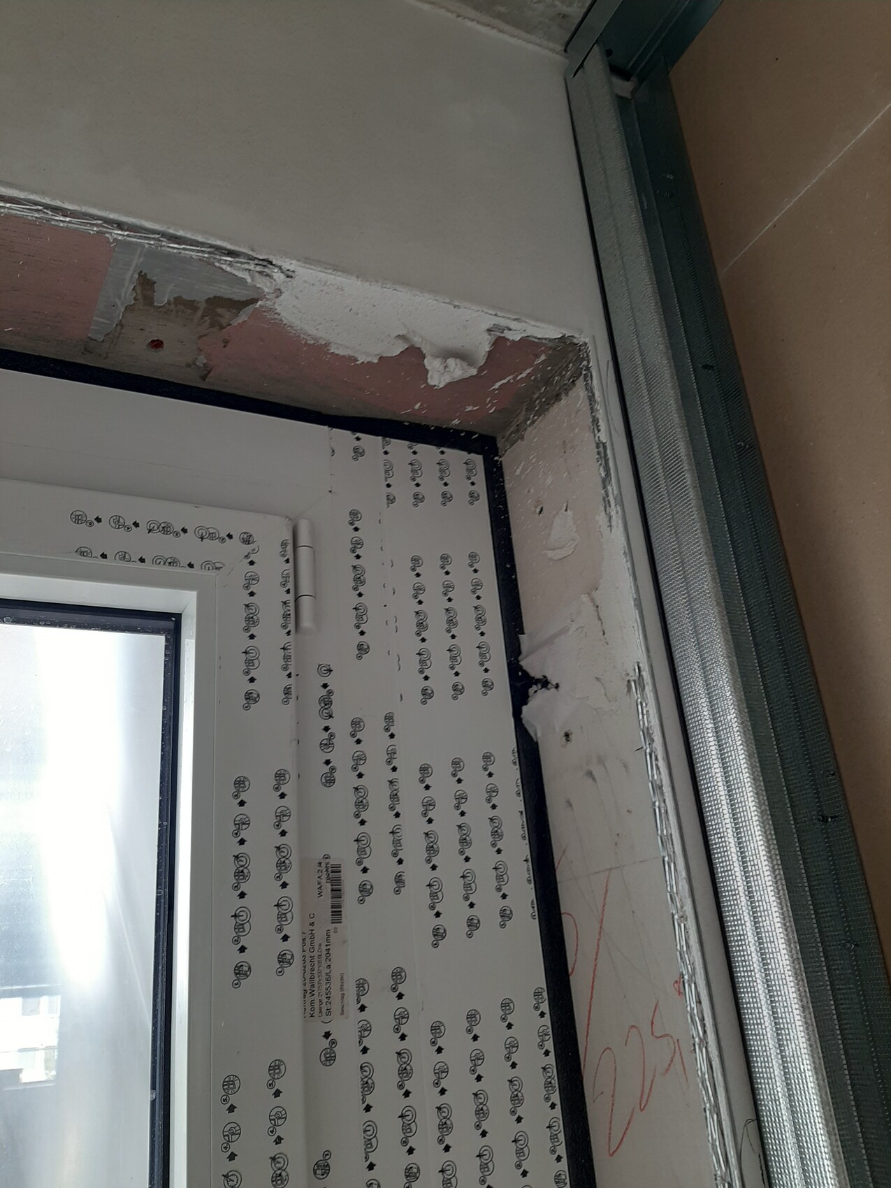 Innenansicht eines Fensterrahmens in Renovierung; Putzschäden über dem Rahmen, Schutzfolie am Rahmen