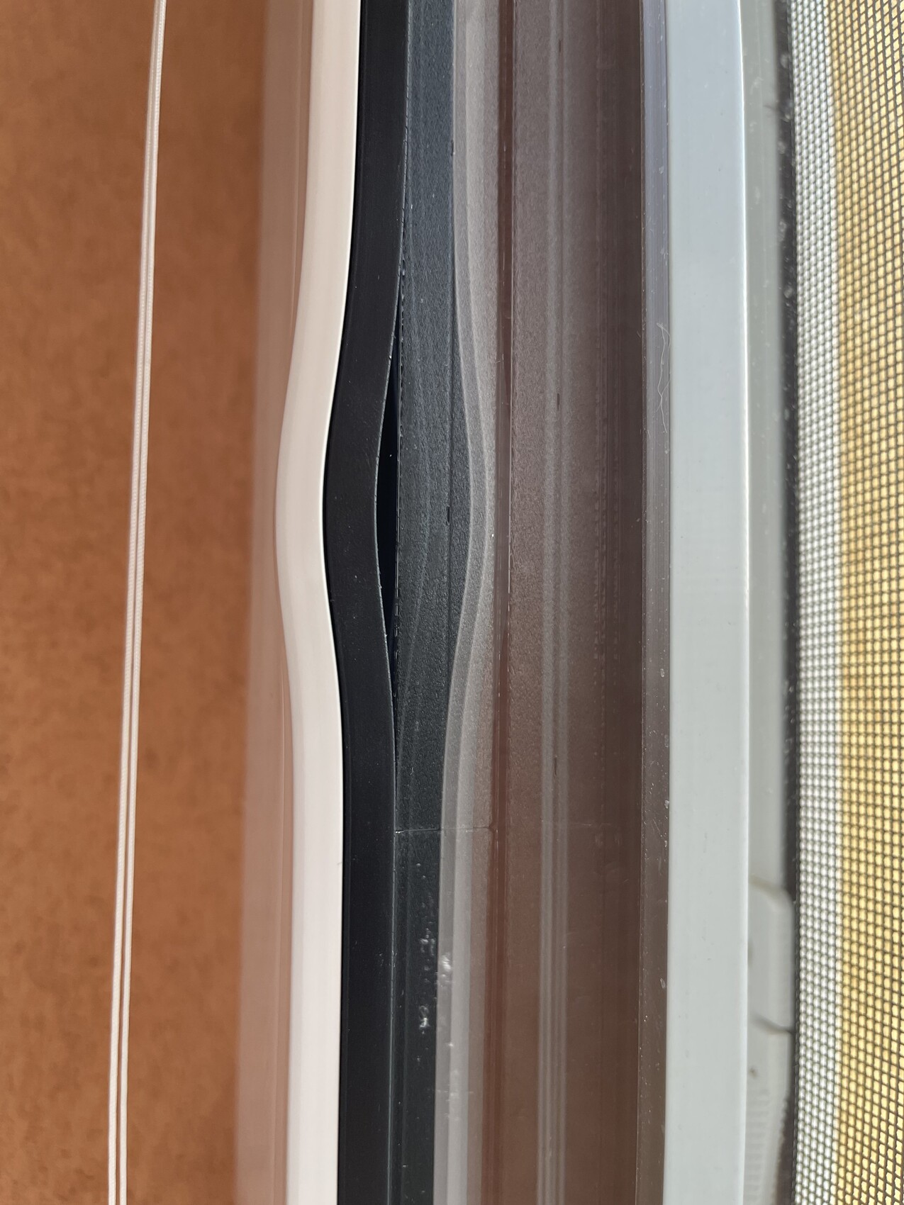 Seitenansicht eines Fensterrahmens mit schwarzen Profilen, weißen Dichtungen und Insektenschutzgitter.