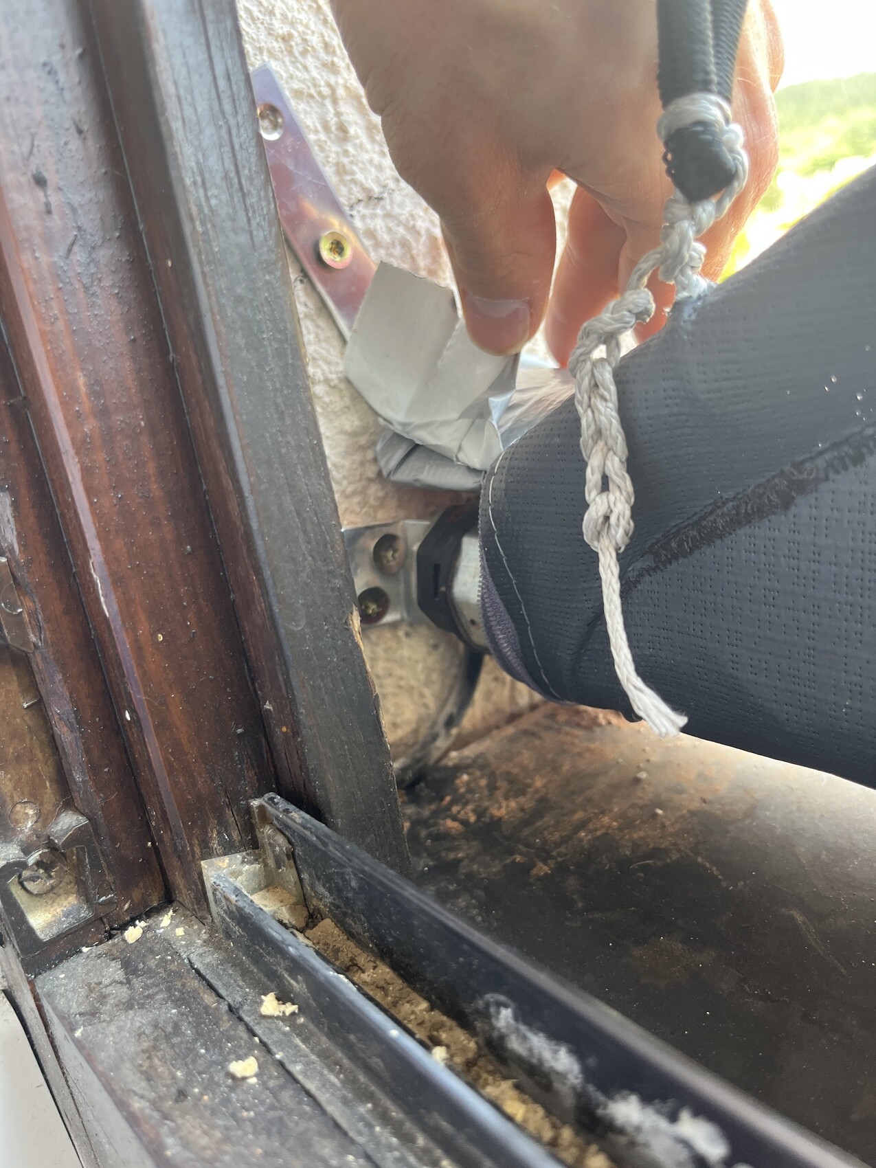 Hand greift eine geflochtene weiße Schnur neben dem Fensterrahmen; Staub am Boden sichtbar.