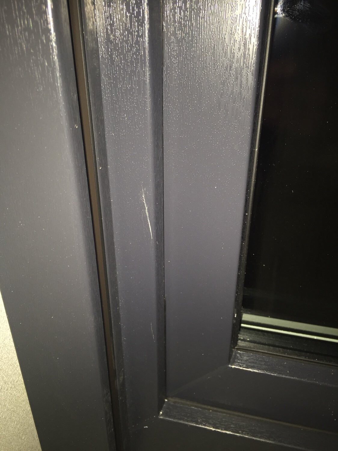 Nahaufnahme eines dunklen Fensterrahmens mit Kratzern und Staub.