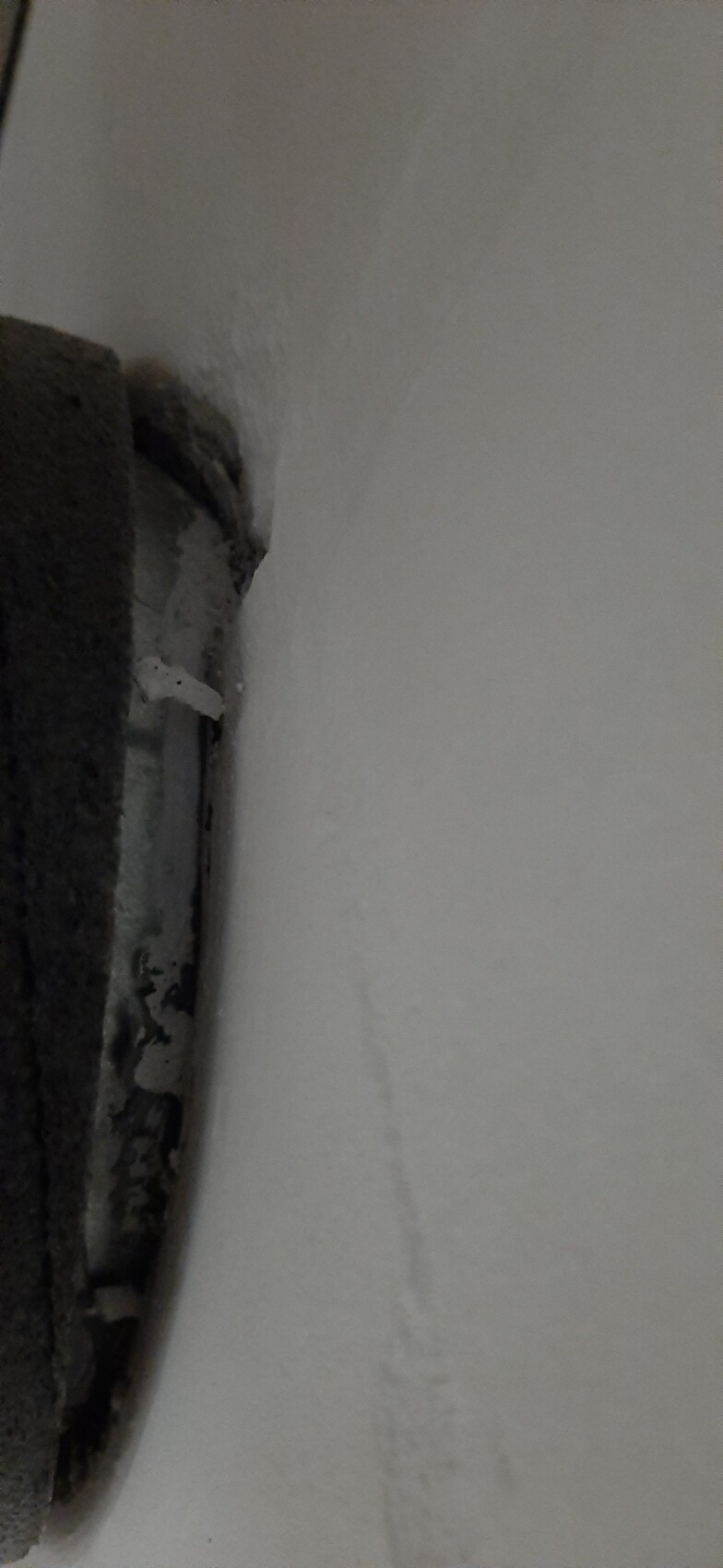 Nahaufnahme einer weißen Wand neben einer dunklen, runden Metallöffnung am linken Rand.