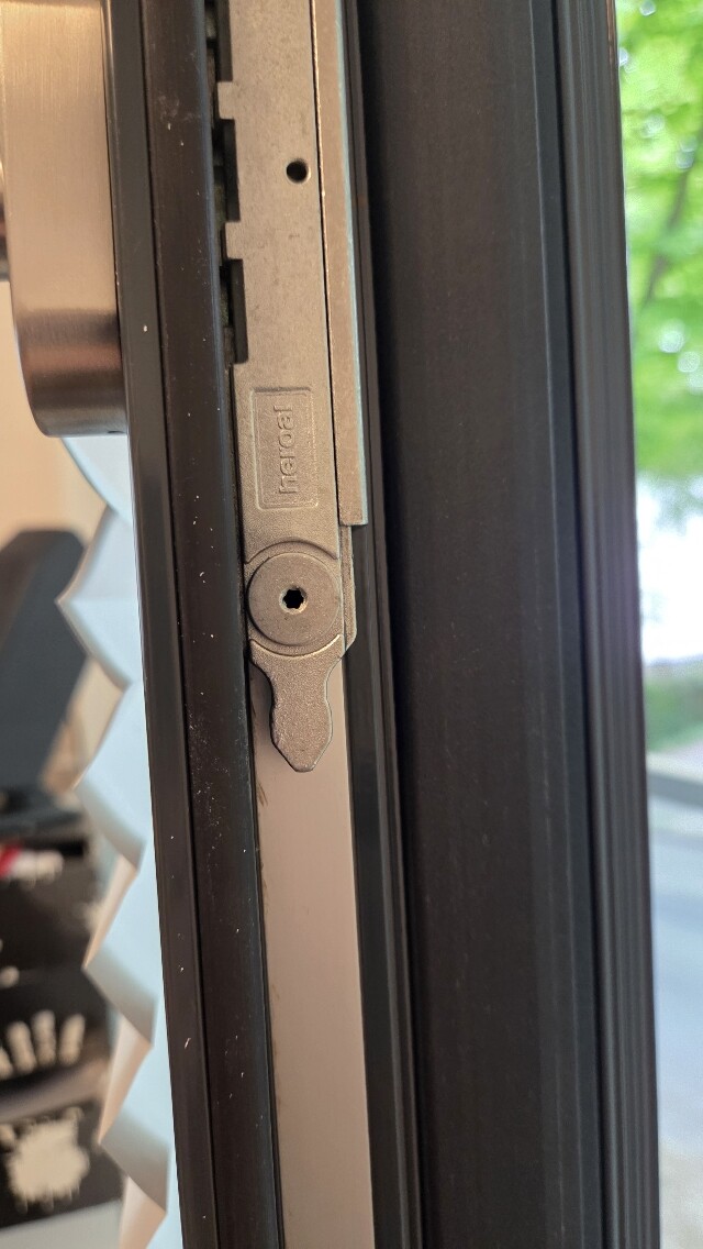 Nahaufnahme eines Fensterschlosses am Rahmen, Metallteil mit Loch, Außen grün.