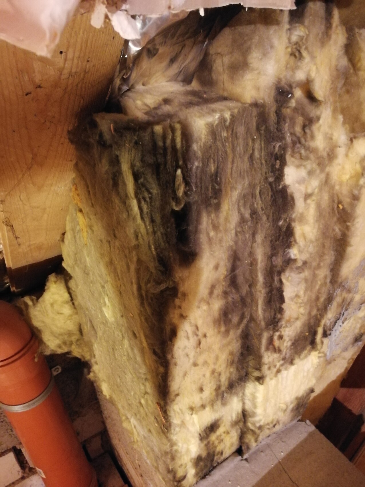 Gelbe Mineralwolle-Isolierung in einer Wand, daneben ein orangefarbenes Rohr.