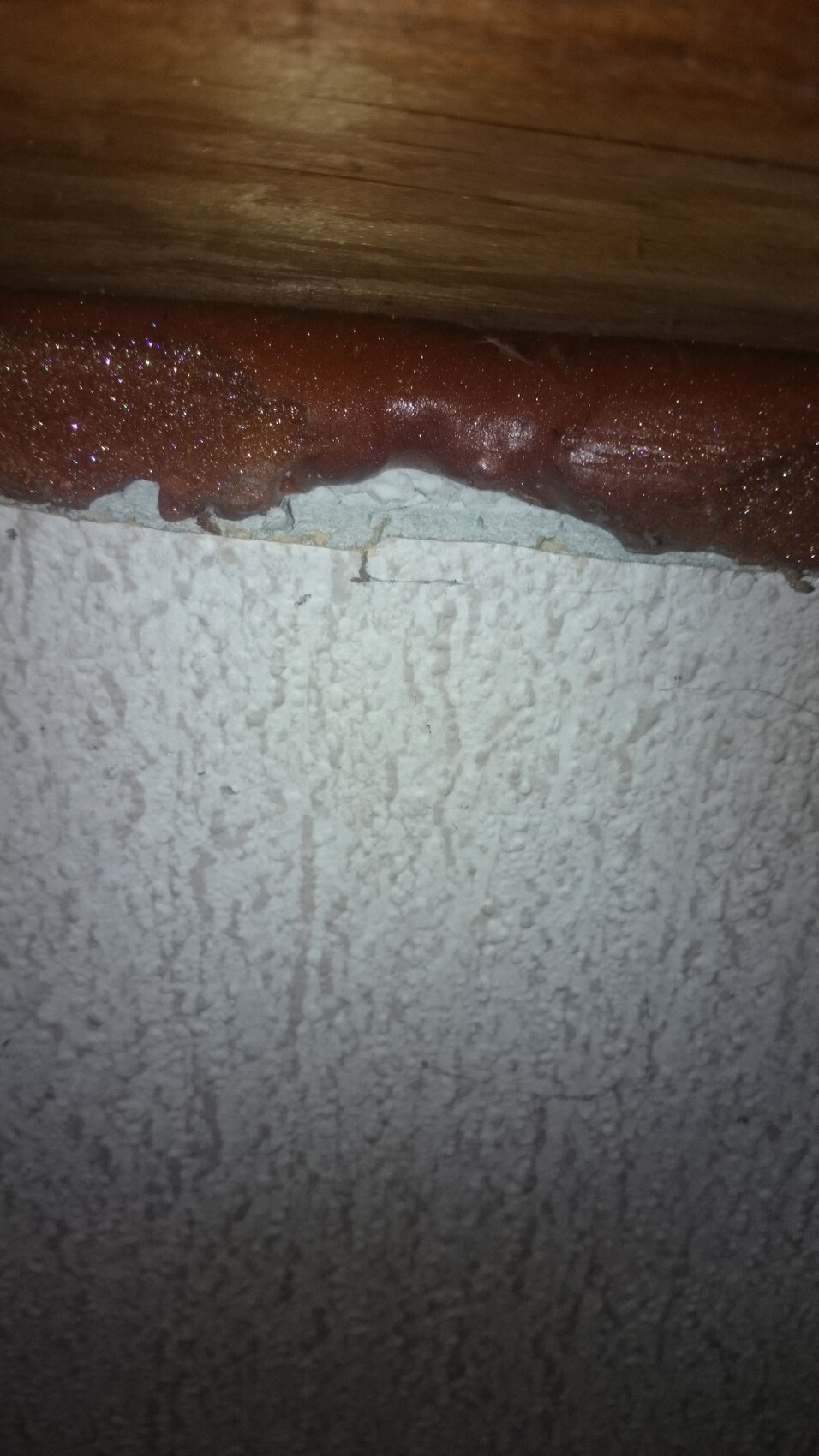Rötlich-braune klebrige Substanz an der Kante zwischen Holzleiste und rauer weißer Wand.
