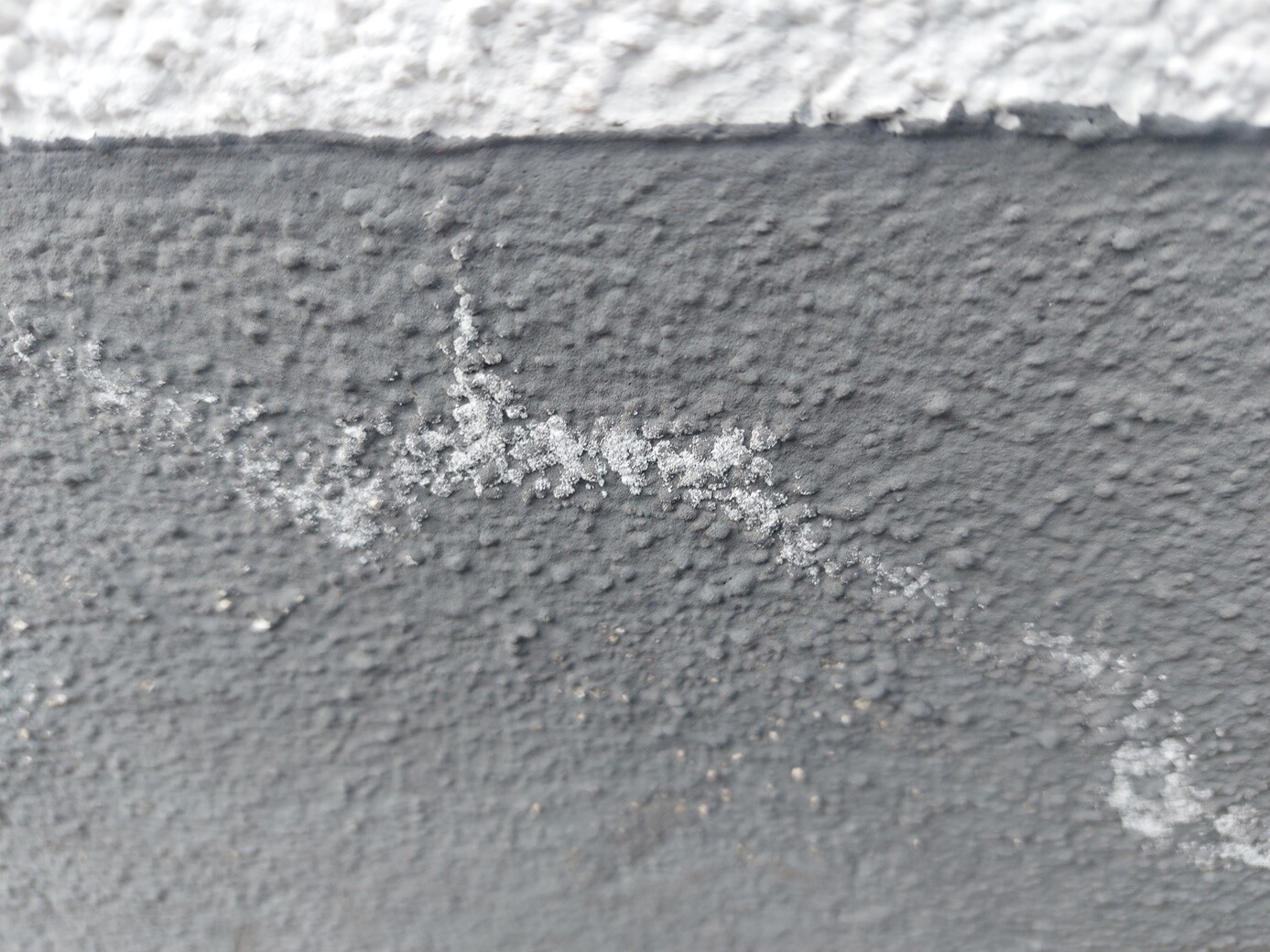 Nahaufnahme einer rauen grauen Wand mit kristallartigen Ablagerungen.