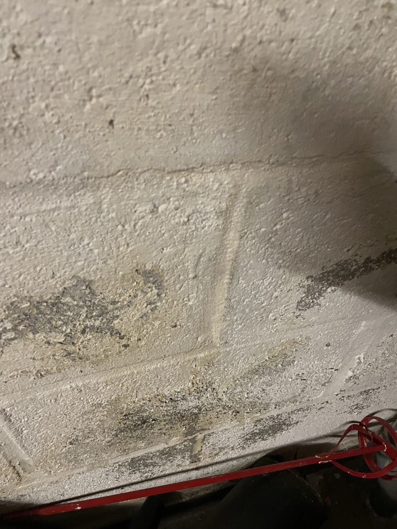 Rauhe, staubige weiße Wand mit Putzabbröckelungen; rotes Kabel am Boden.