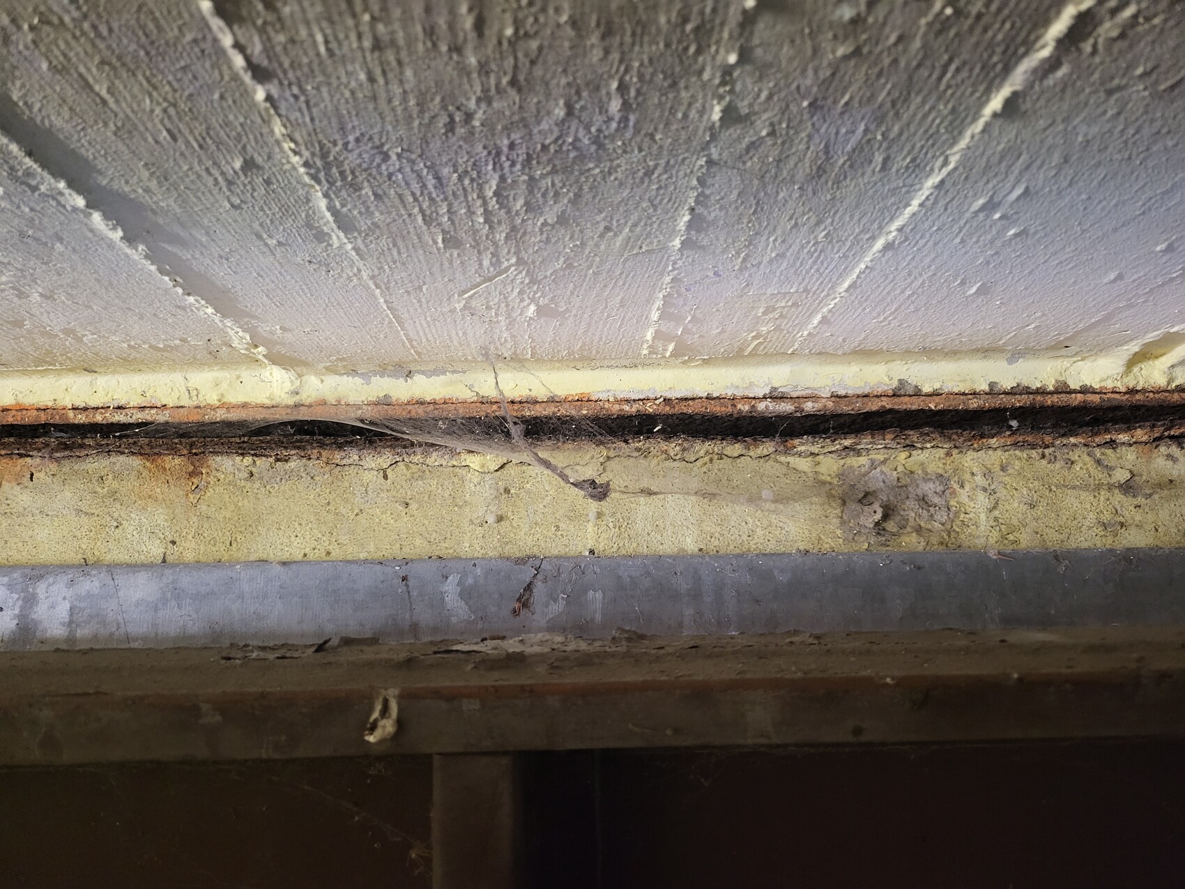 Nahaufnahme eines staubigen Spalts zwischen Wand und Boden, rostige Metallkante, Spinnennetz.