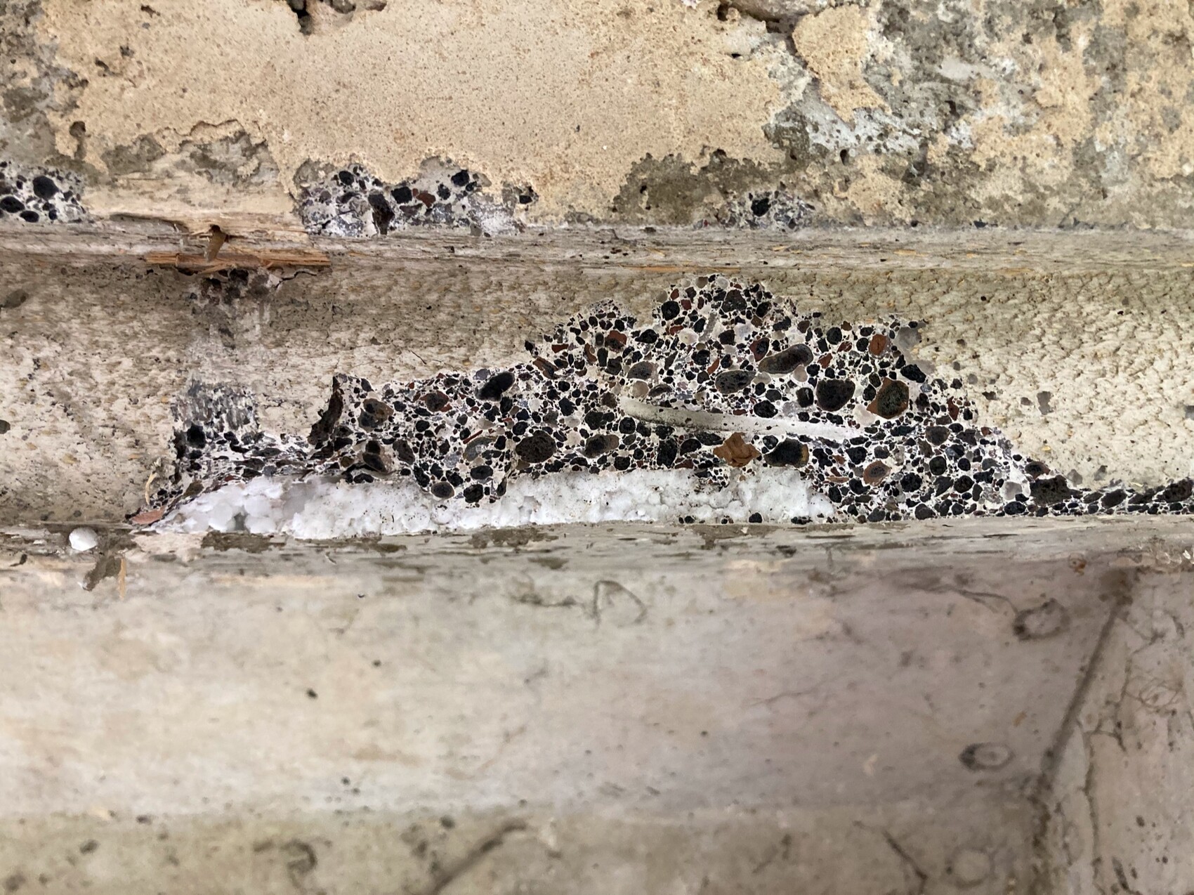 Eine Betonwand mit Riss, durch den ein Patch aus dunklen Kieselsteinen sichtbar ist.