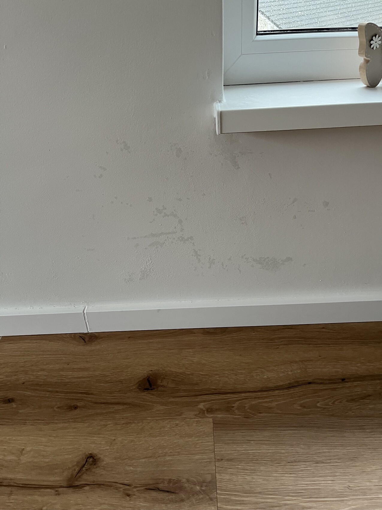 Innenwand mit feuchten Flecken unter dem Fenster, weißer Sockel und Holzboden.
