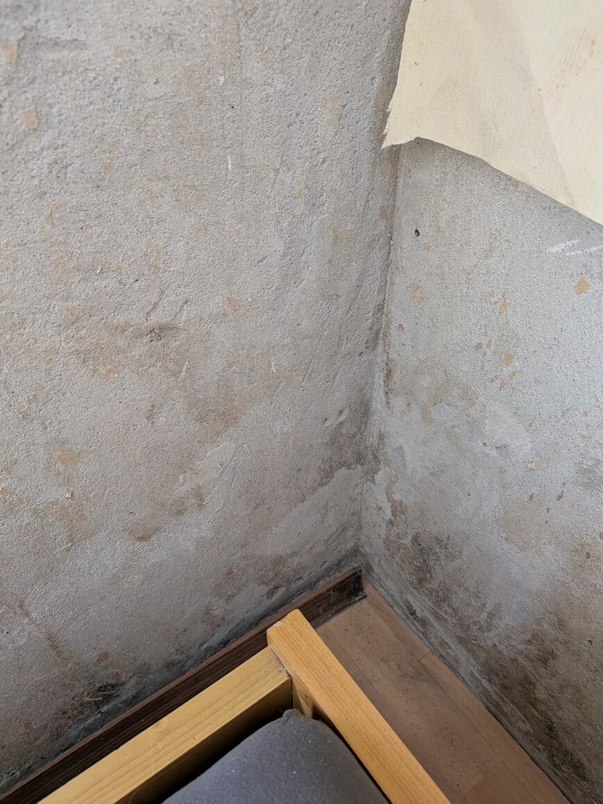 Kellerwand mit Feuchtigkeit und Verputzschaden in der Ecke.
