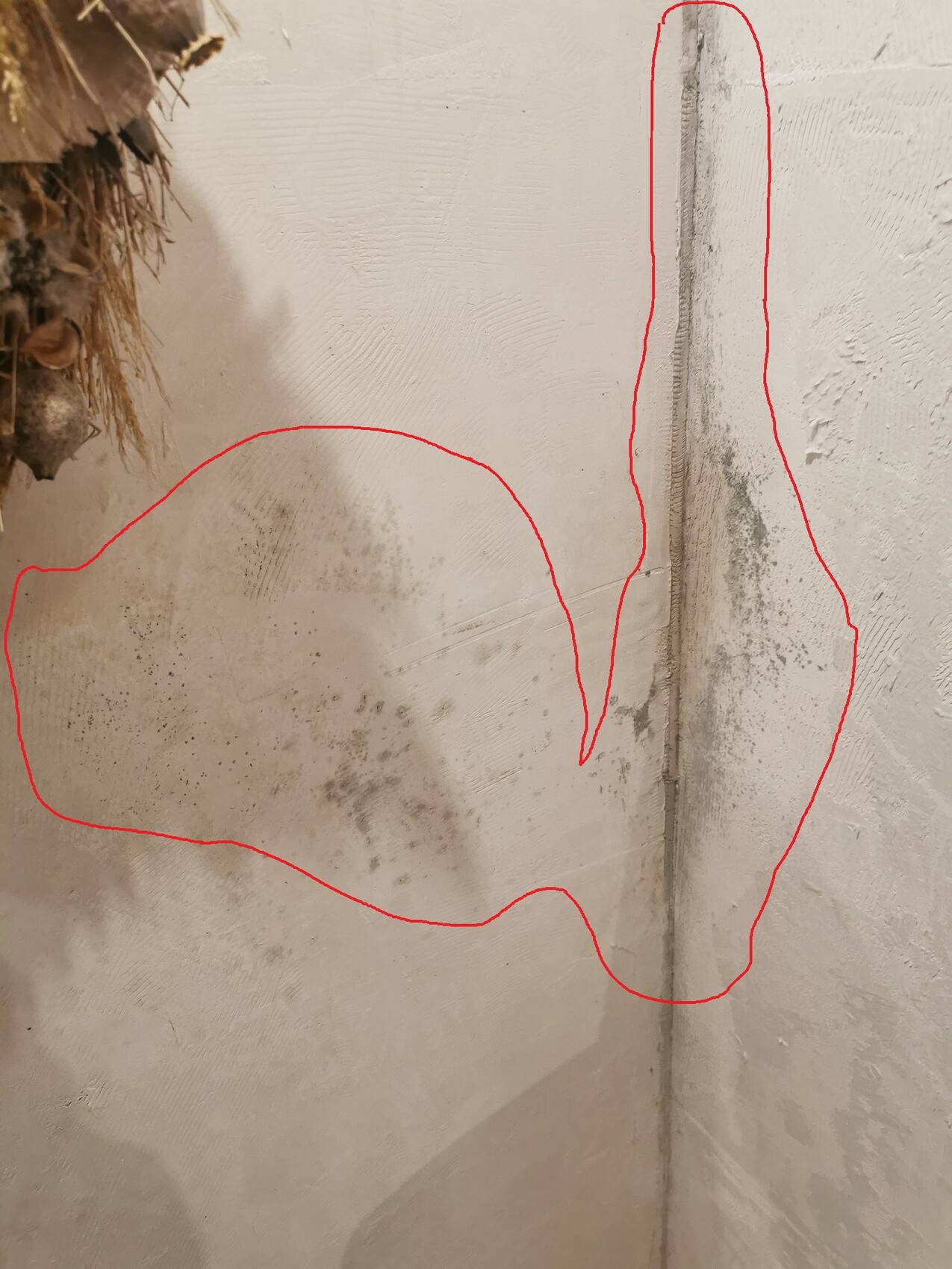 Weiße Putzwand mit grauen Flecken, vertikale Fuge rechts; oben links Stroh-Deko.
