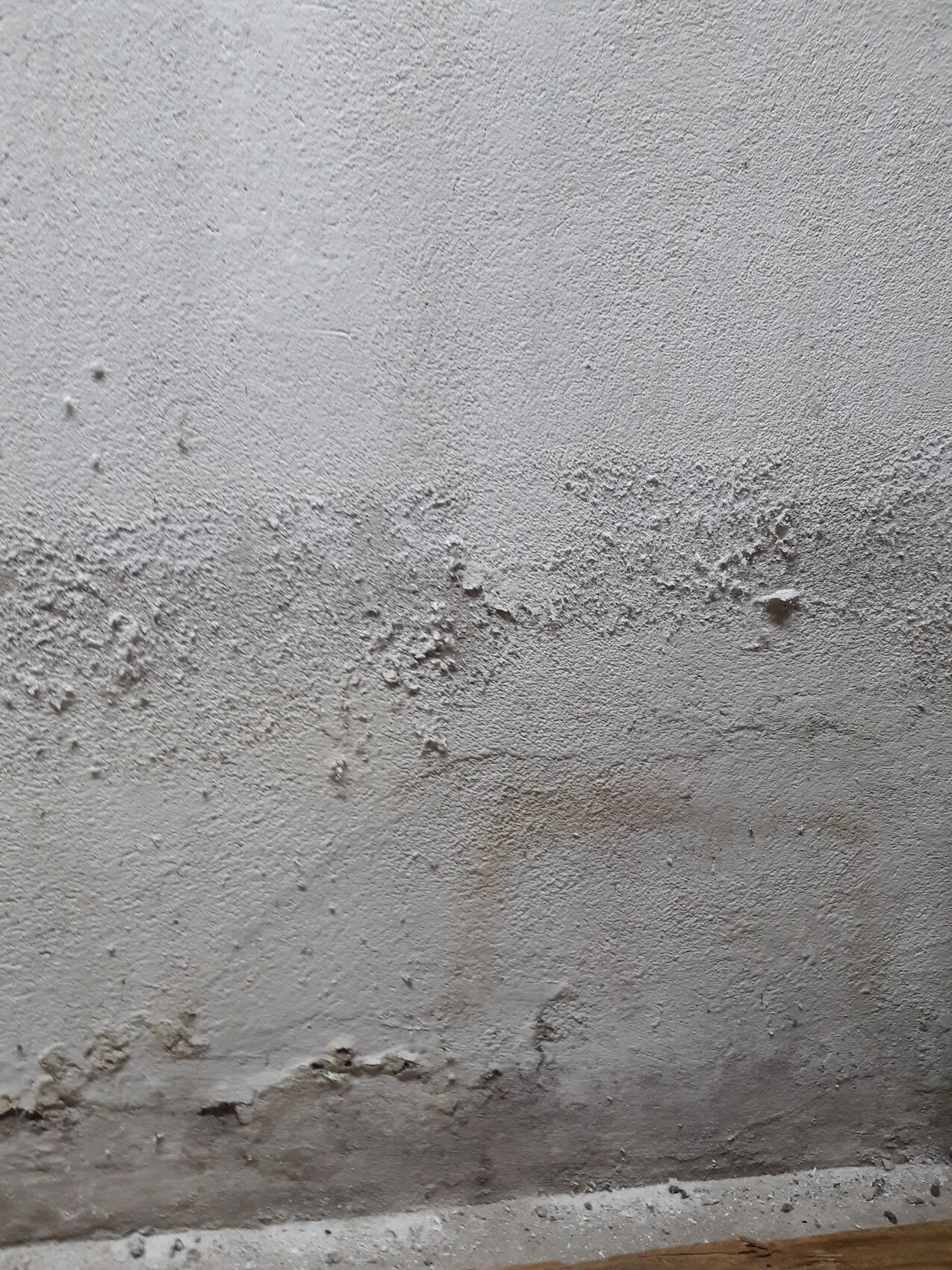 Grau verputzte Wand mit rauer Struktur und Feuchtigkeitsspuren am unteren Rand.
