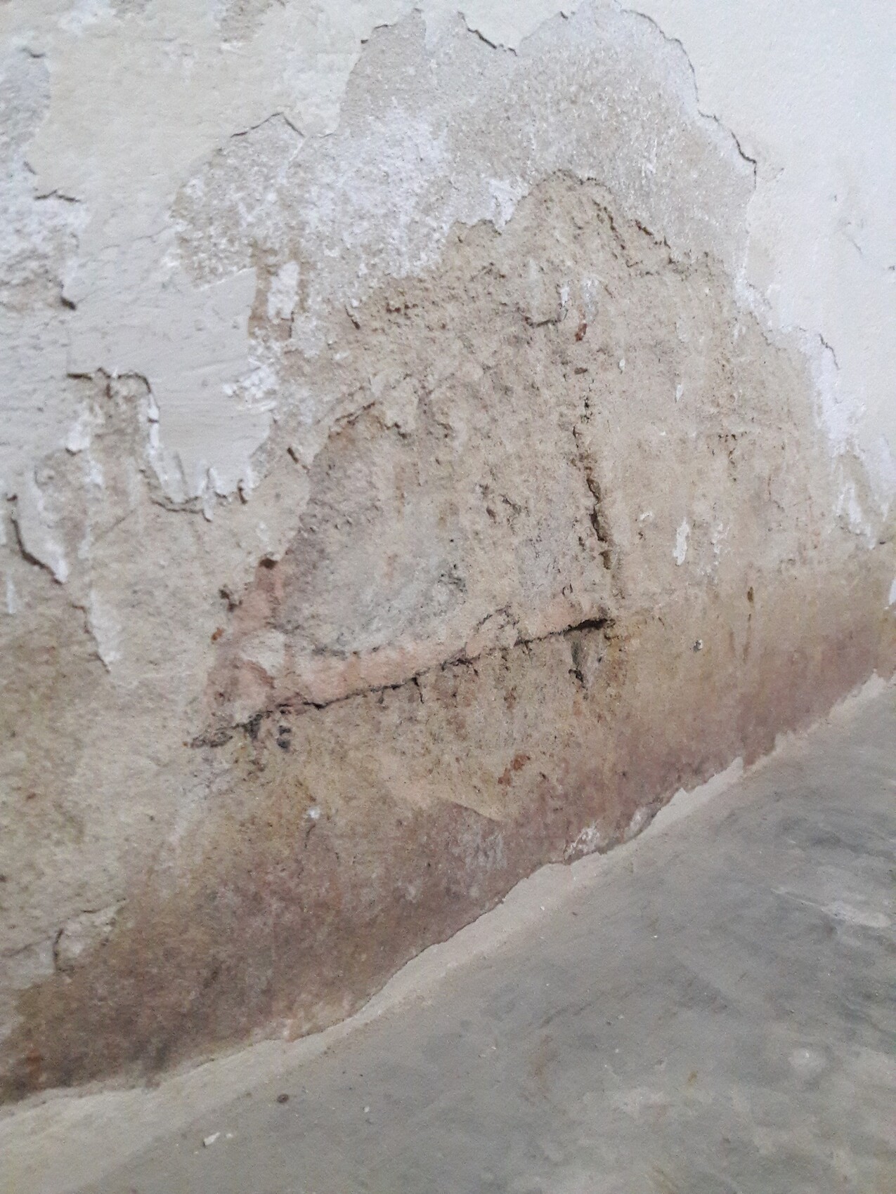 Abgeblätterte Putzwand mit Feuchtigkeitsschaden am unteren Rand.