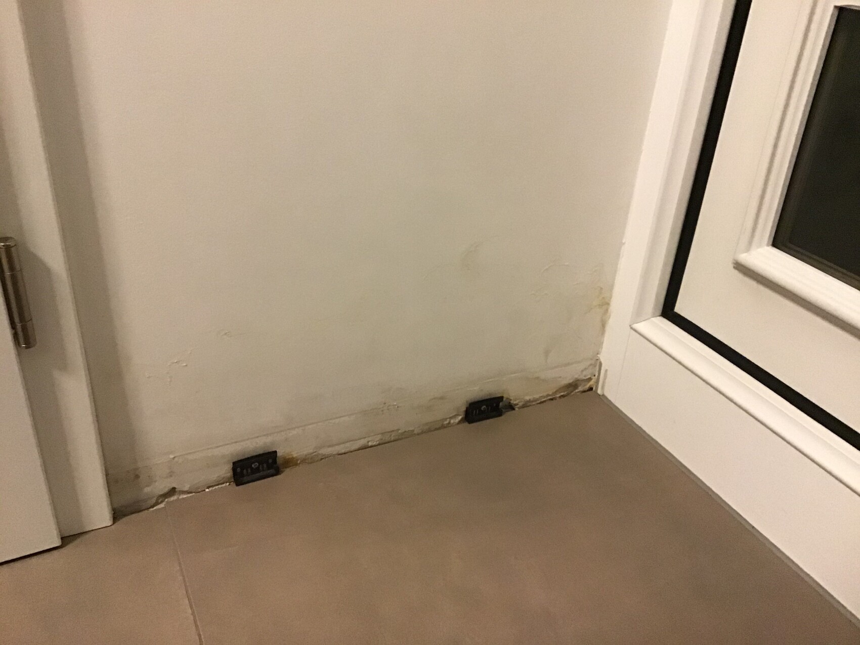 Eckwand mit Fenster rechts; feuchte Wand unten, Abplatzungen, zwei Steckdosen an der Fußleiste.
