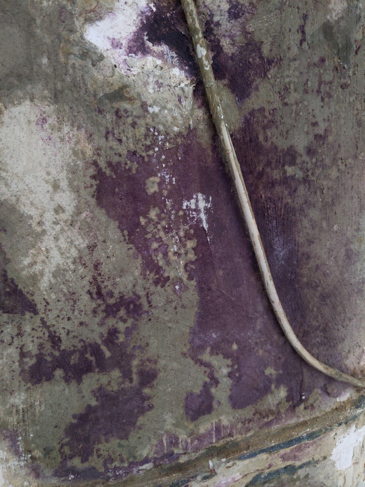 Graue Wand mit violetten Verfärbungen und einer an der Wand hängenden Schnur