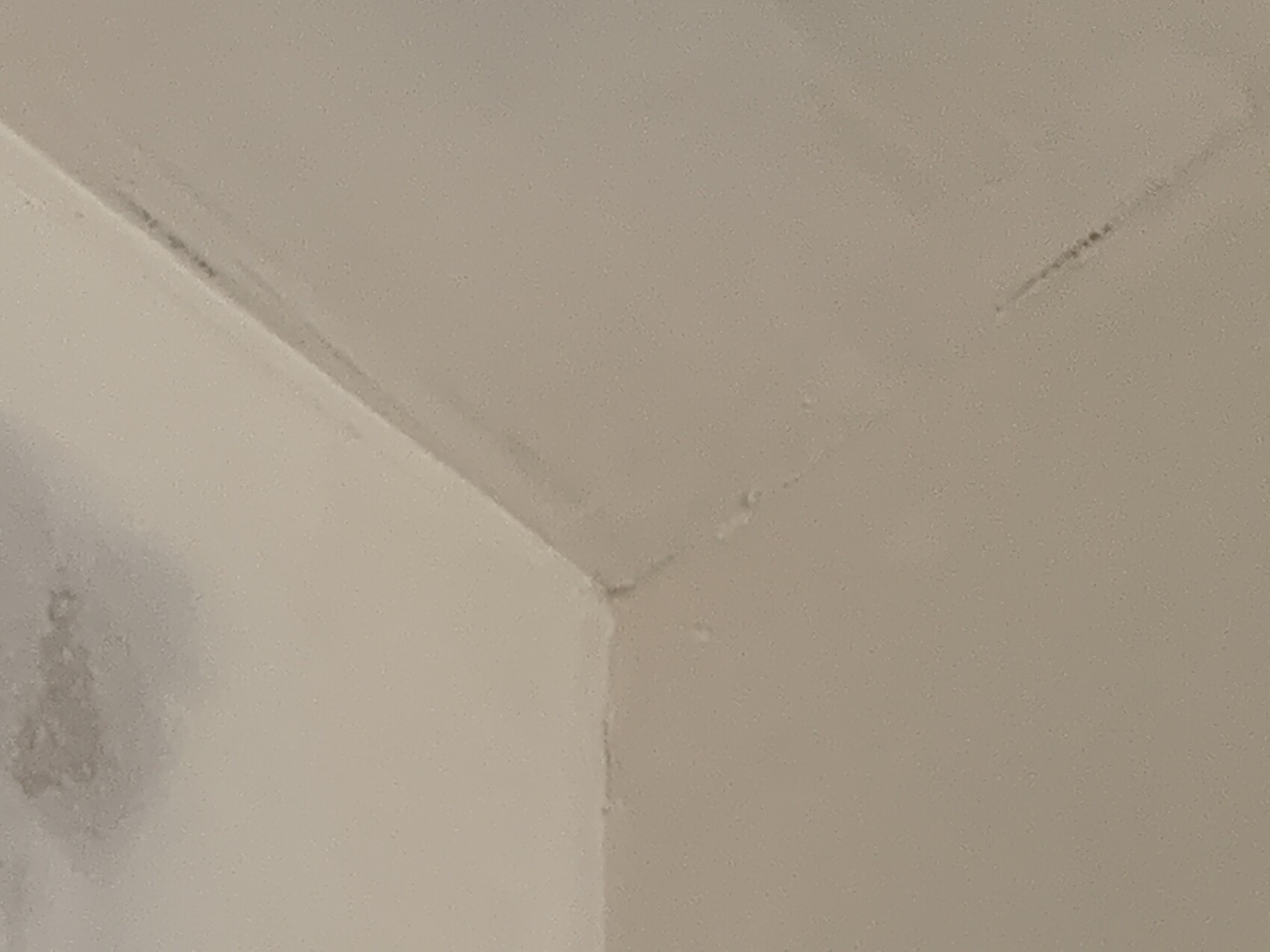 Weiße Decke und Wand-Ecke mit Risslinien, links unten Fleck