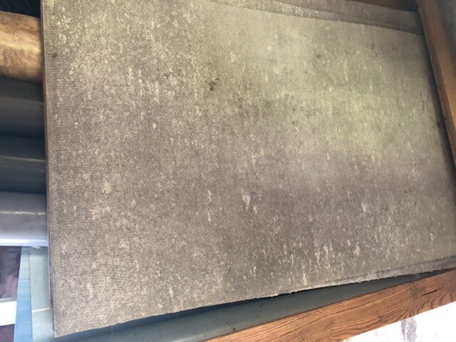 Staubige, grünlich-graue Metallplatte mit Flecken, von Holzrahmen eingefasst.