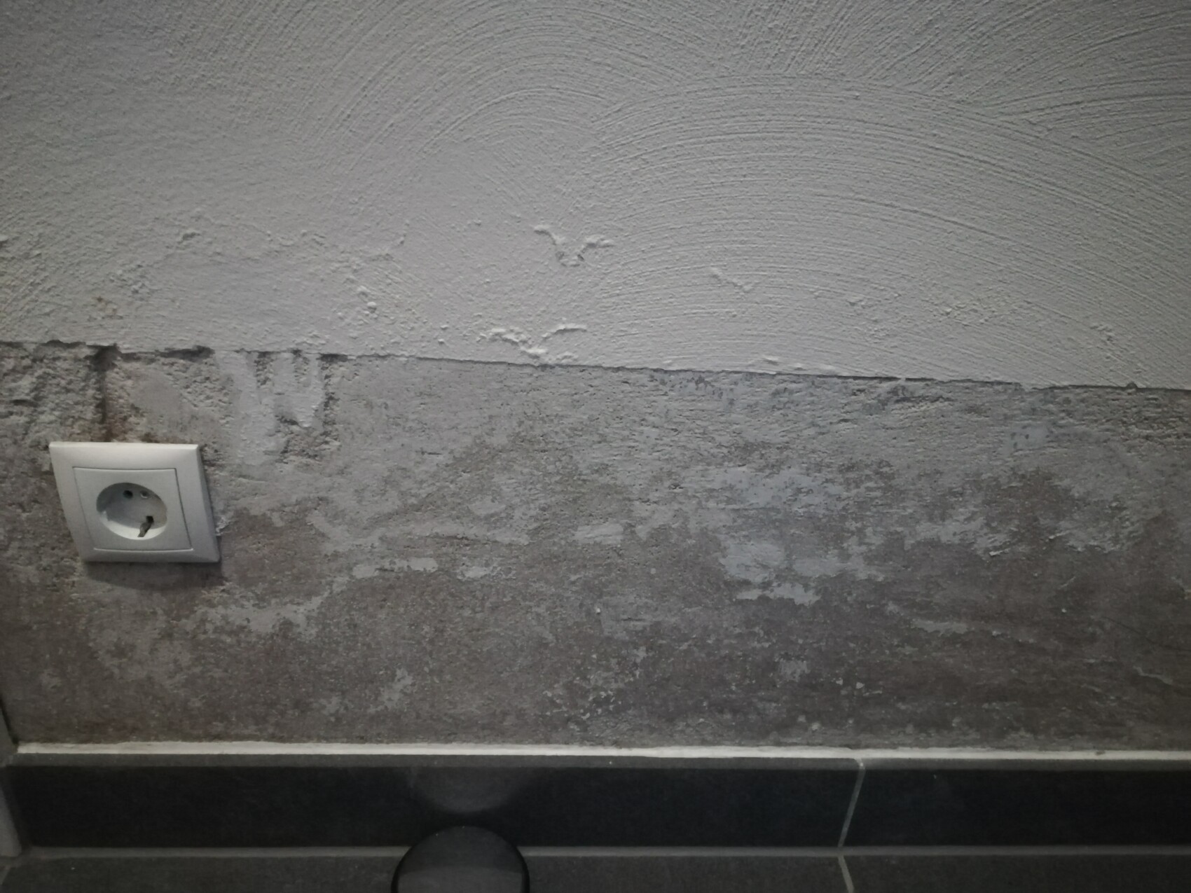 Helle verputzte Wand oben, dunkle grobe Wand unten; links unten eine weiße Steckdose.