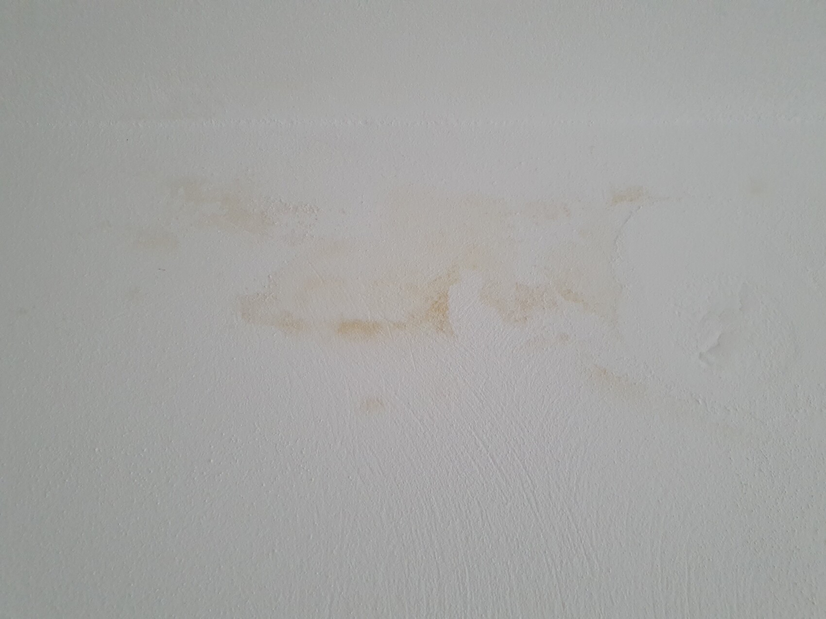 Weiße Wand mit Textur und braunen Flecken in der Mitte.