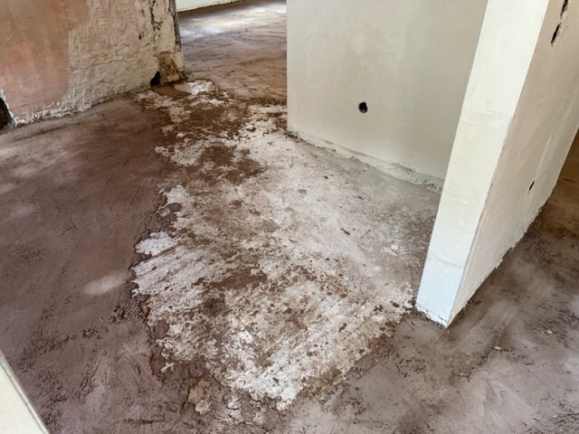 Innenraum eines Bauwerks; Boden mit Putzresten, weiße Stützwand rechts, offener Hintergrund
