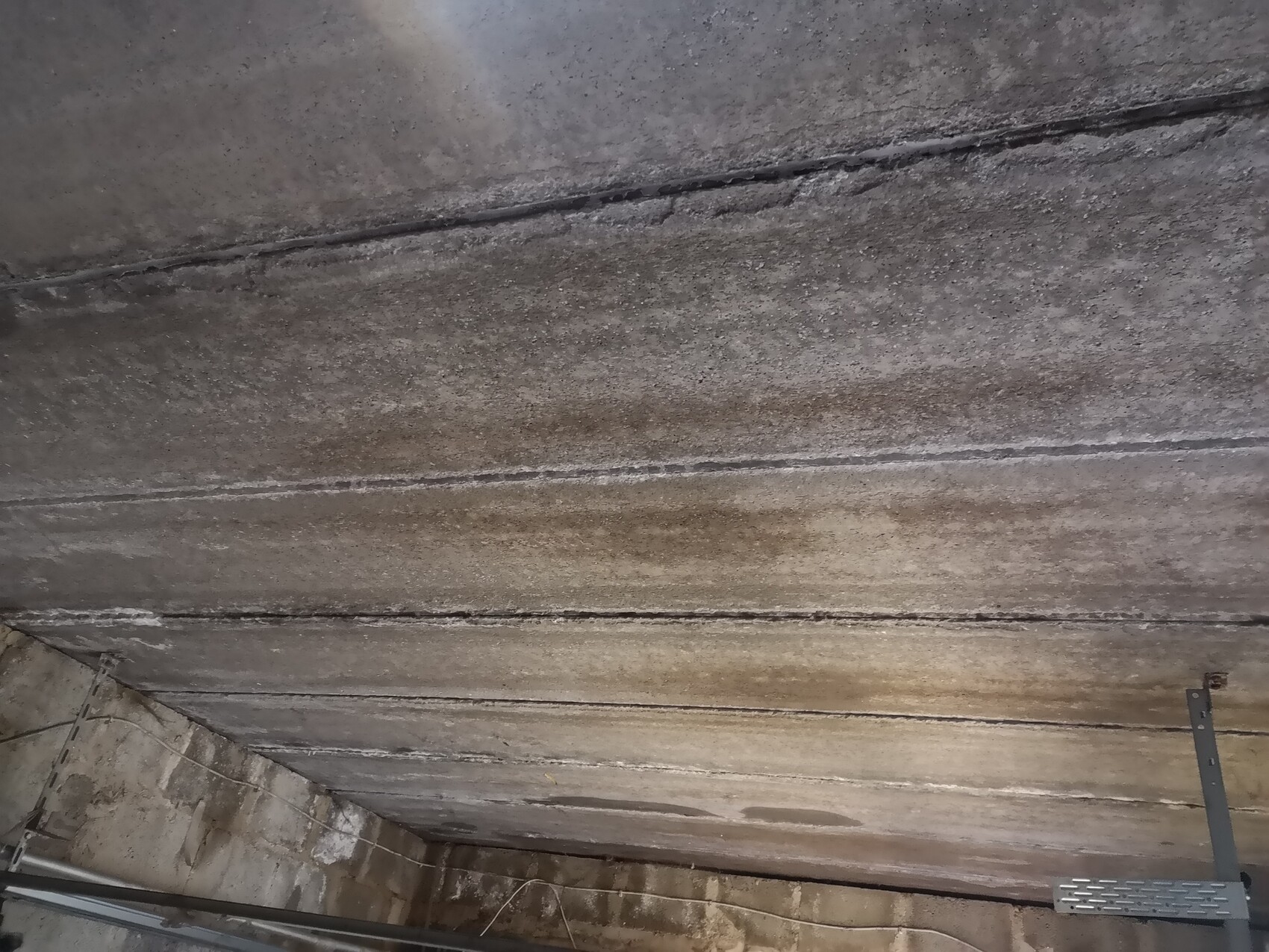 Kellerbetondecke mit Feuchtigkeit, dunkeleren Streifen und sichtbaren Metallträgern