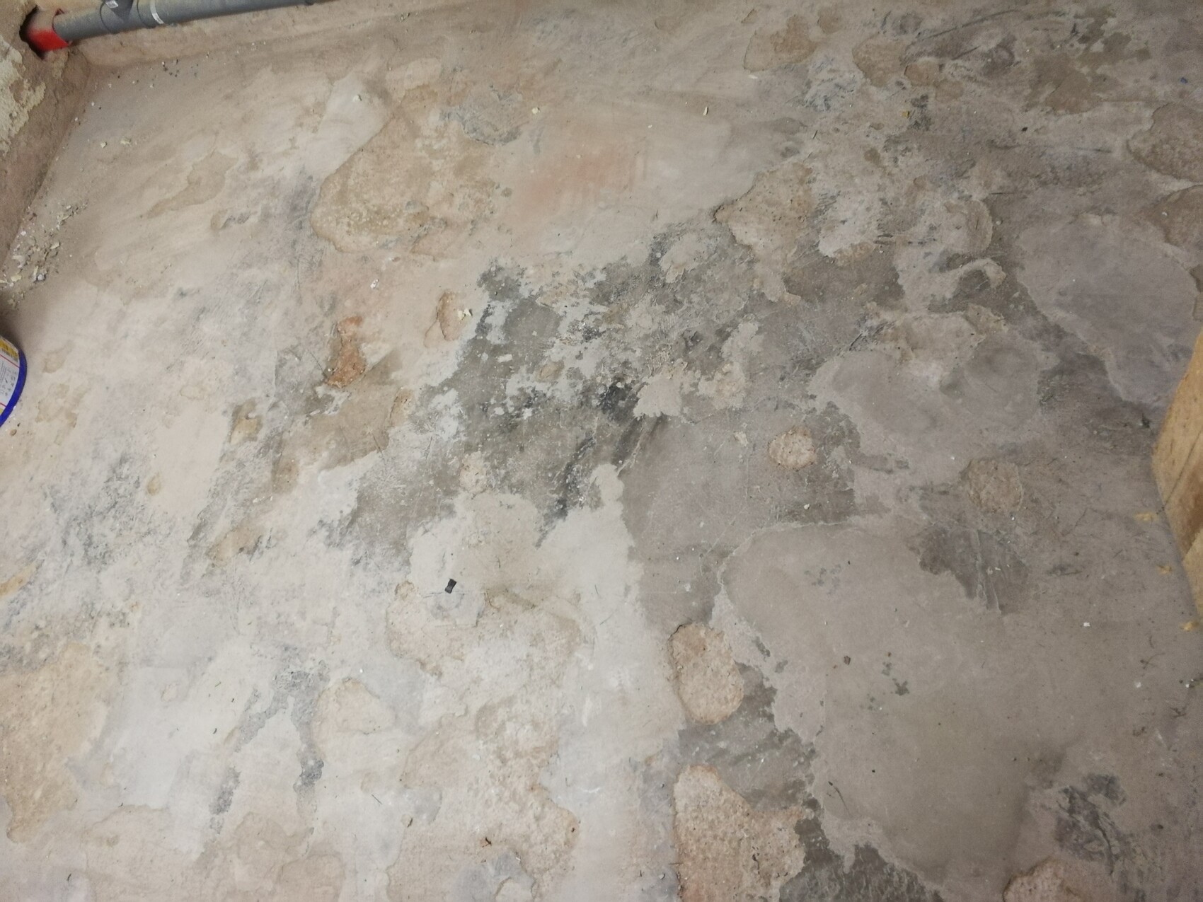 Abgenutzter Betonboden mit Flecken und Feuchtigkeit; Abplatzungen; Rohr oben links.