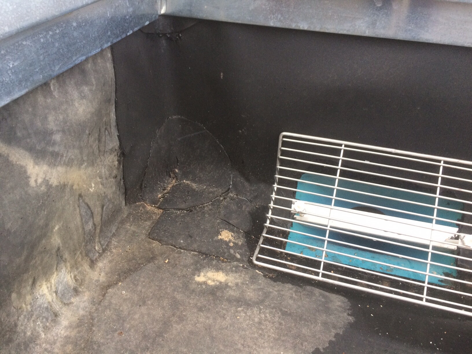 Dunkler Innenraum eines Grills mit Ruß; ein Metallgrillrost liegt schräg auf einer blauen Basis.