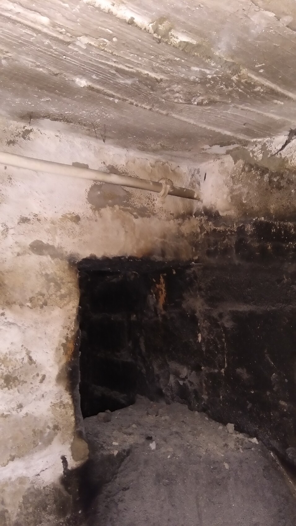 Kellerraum mit rauer Wand, Rohr an der Decke, dunkle Öffnung in der Wand, staubiger Boden.