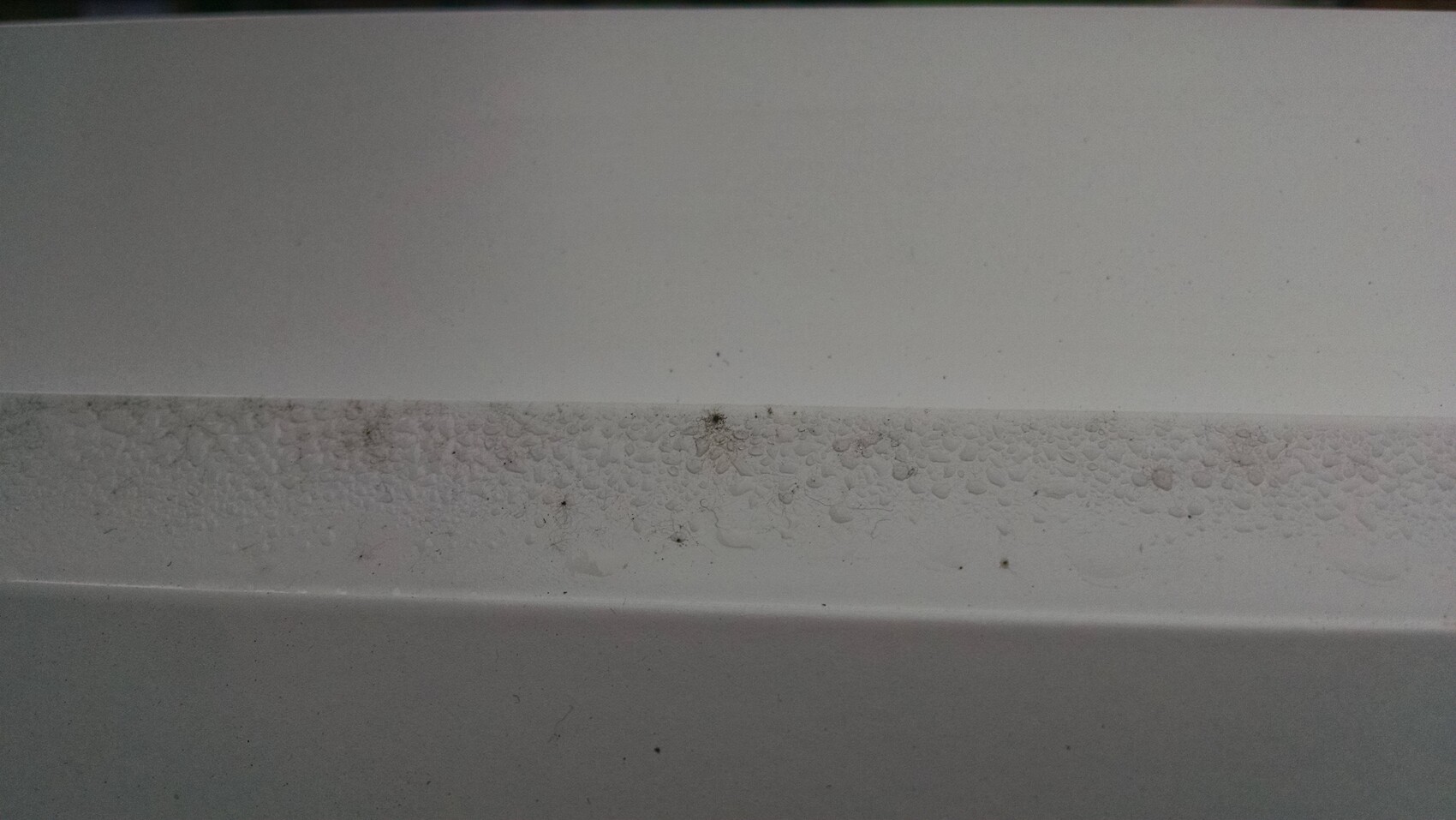 Weiße Wand mit Feuchtigkeitsspuren und Schimmel am unteren Rand