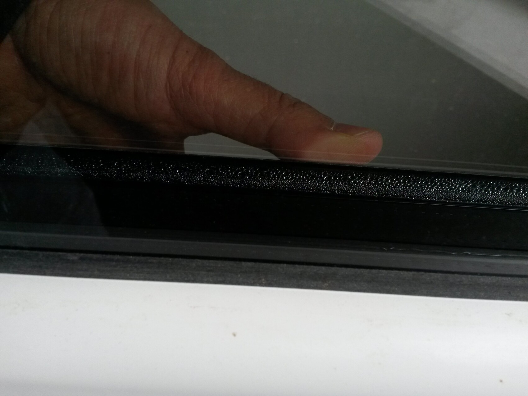 Nahaufnahme einer Hand an einer Fensterdichtung am Fenstersrahmen