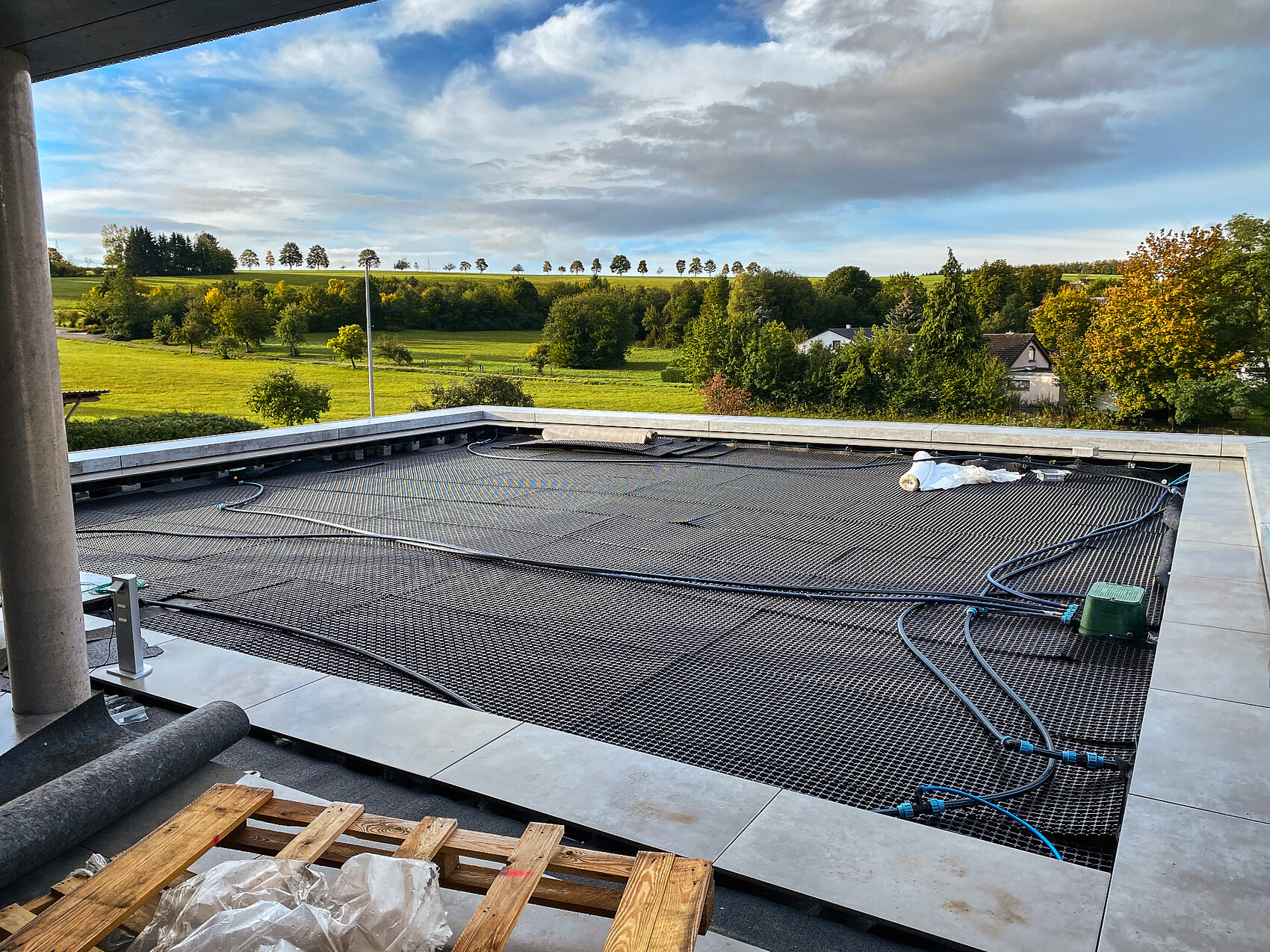 Dachbaustelle mit Metallgitter, Schläuchen; grüne Felder und Häuser im Hintergrund