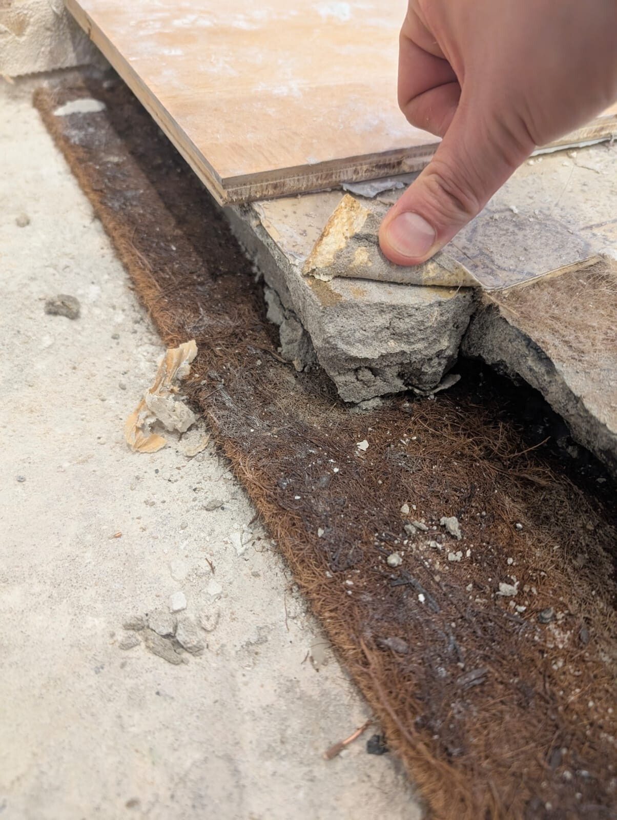Hand legt Holzplatte auf Betonfundament, darunter eine braune Kokosfaser-Matte.