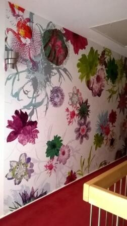 Heller Raum mit bunter Blumen-Wandtapete und rotem Teppichboden.